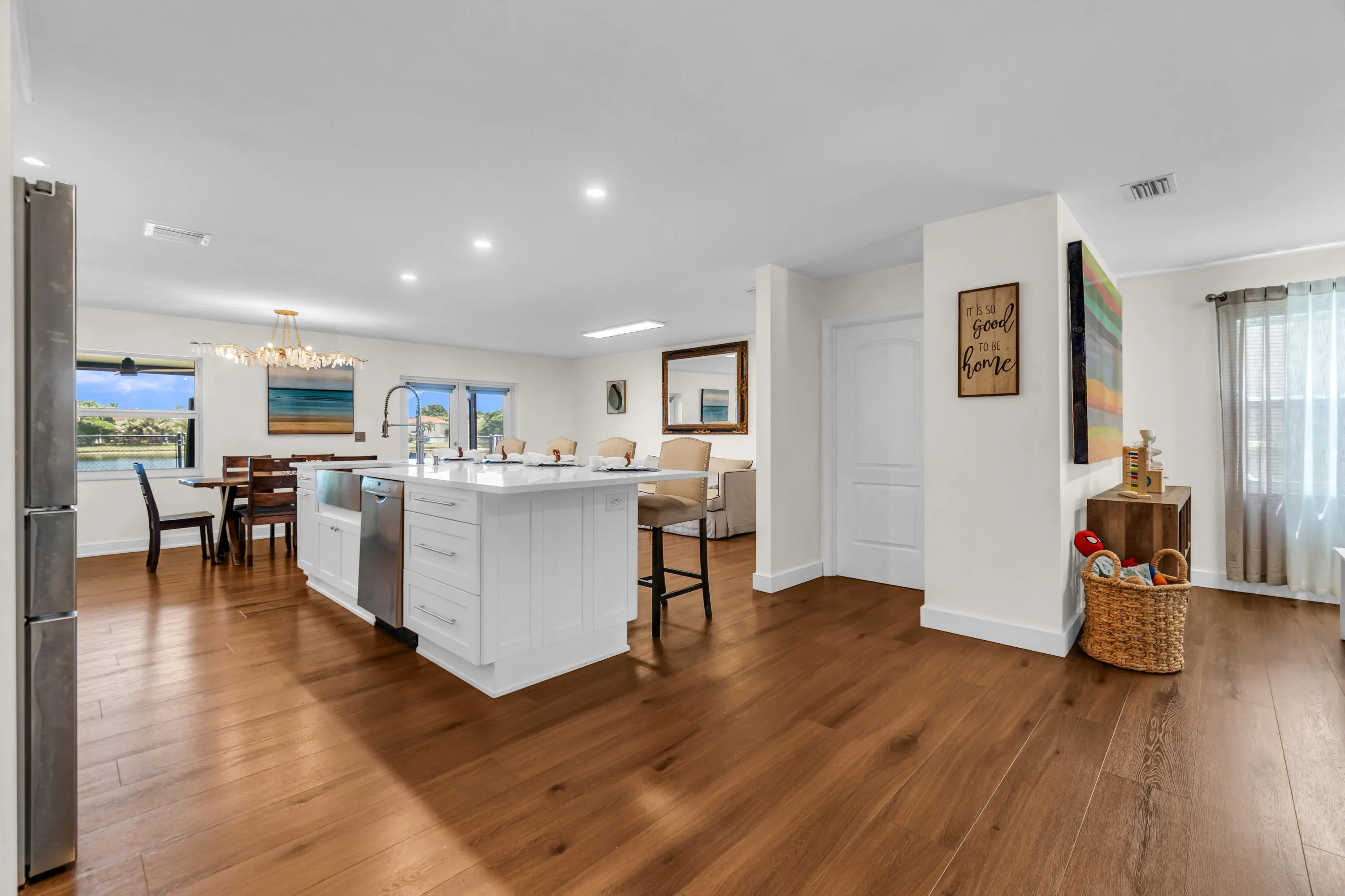 Open-concept space featuring wood-finish flooring, a white kitchen island with integrated stainless steel appliances, recessed lighting, and large windows