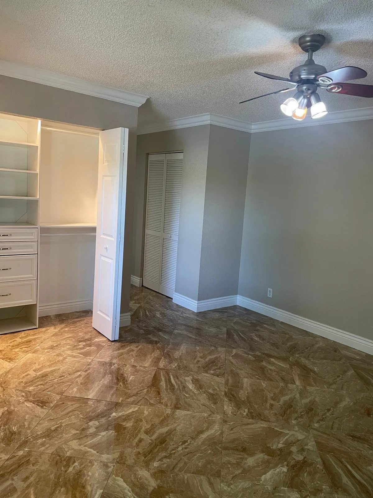Built-in custom closet system with drawers, crown molding, ceiling fan with integrated lighting, textured ceiling, and patterned tile flooring