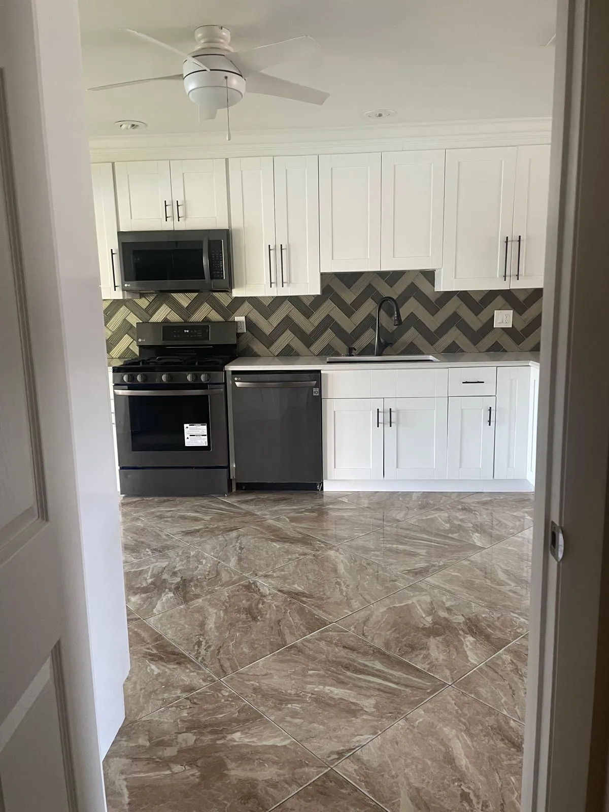 White shaker cabinetry, dark chevron pattern backsplash, black appliances, white countertops, and large format floor tiling