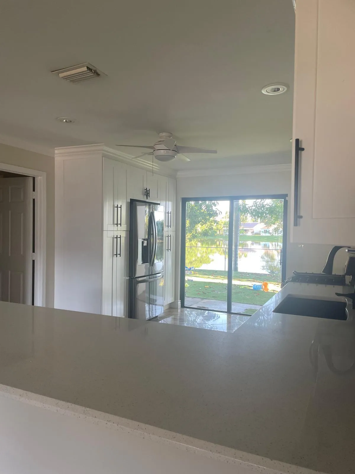 Expansive countertop with an undermount sink, white cabinetry with dark hardware, stainless steel refrigerator, ceiling fan, and sliding glass doors