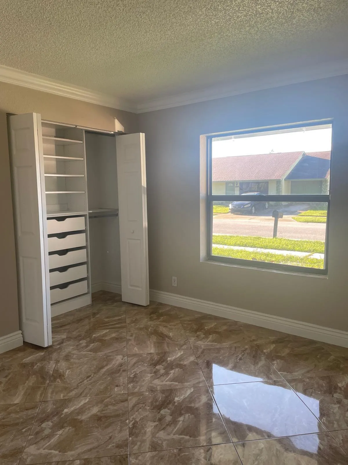 Built-in closet organization system with shelving and drawers, crown molding, large window, and tile flooring