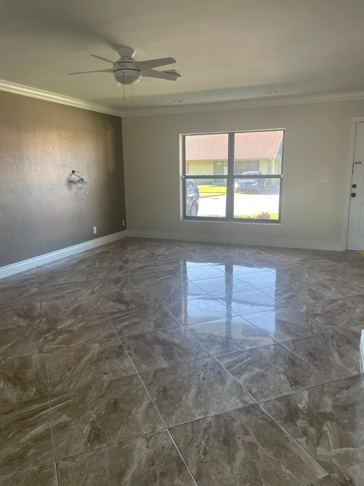 Expansive room featuring large format tile flooring, crown molding, a ceiling fan, and a double-pane window