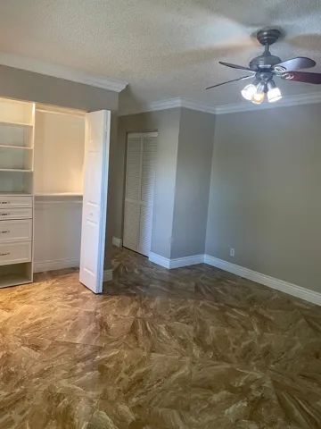 Built-in custom closet system with drawers, crown molding, ceiling fan with integrated lighting, textured ceiling, and patterned tile flooring