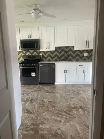 White shaker cabinetry, dark chevron pattern backsplash, integrated appliances, ceiling fan, and large format floor tiling