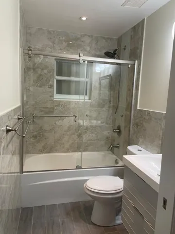 Bathroom featuring a tub/shower combination with sliding glass doors, full-height tile surround, and an integrated window