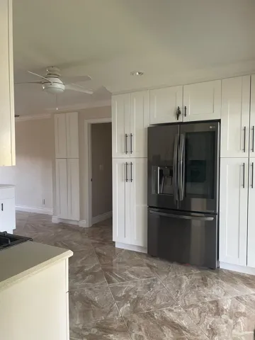 White shaker-style cabinetry with dark hardware, stainless steel refrigerator, tile flooring, and ceiling fan