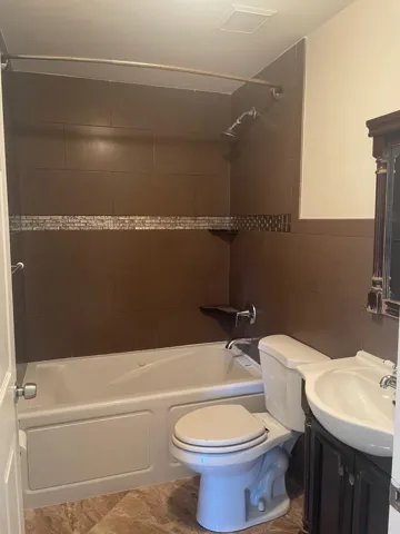 Built-in bathtub with a shower featuring brown wall tiles and a decorative mosaic accent