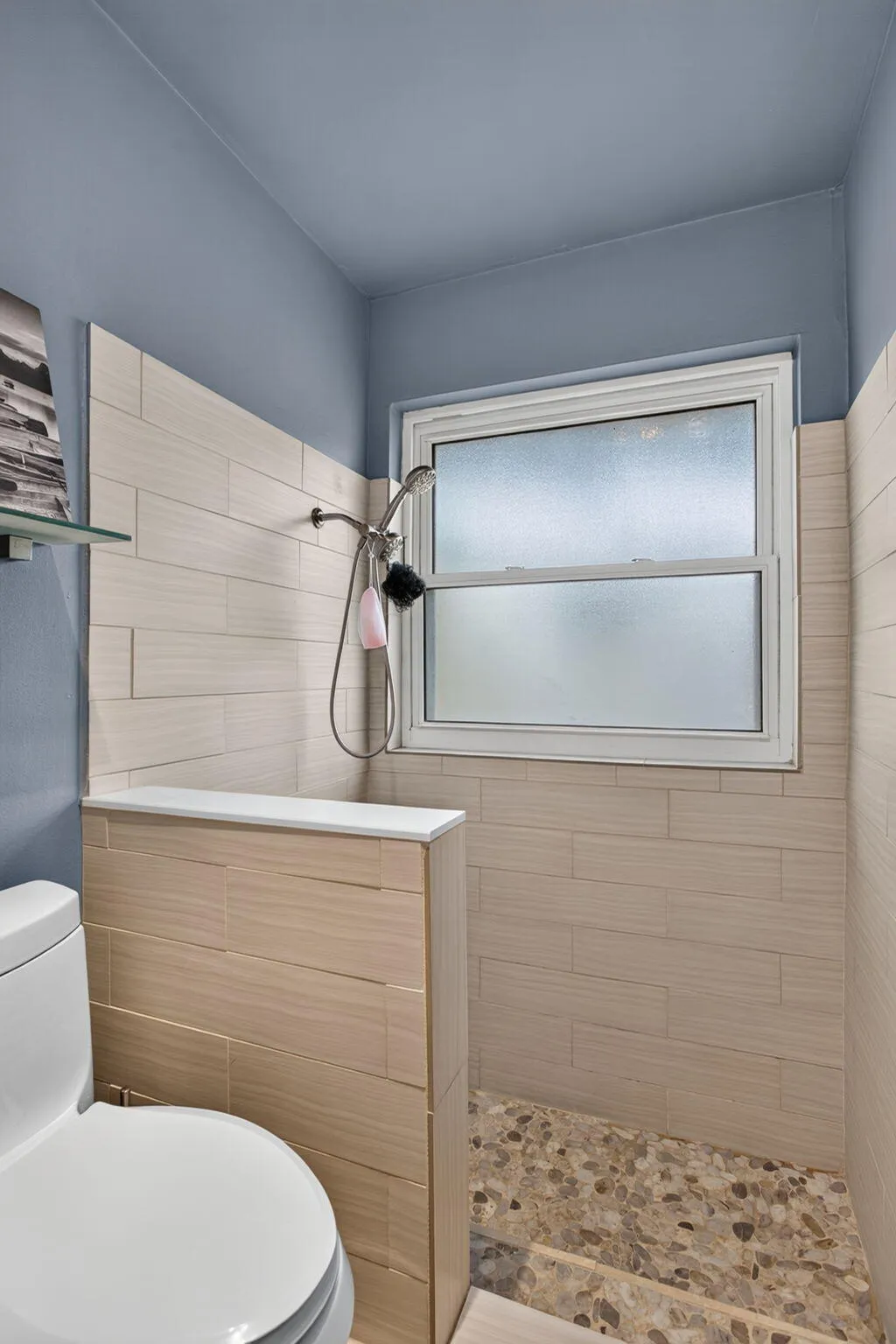 Bathroom featuring a walk-in shower with pebble tile flooring, light-toned horizontal wall tiles, and a frosted glass window