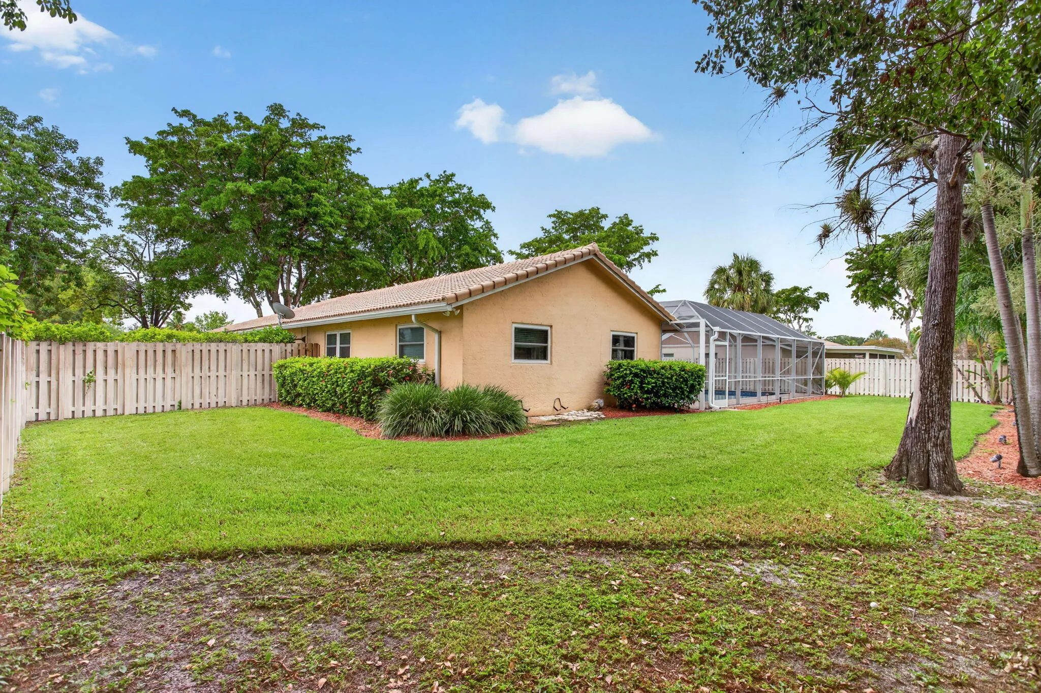 Expansive backyard with a screened pool enclosure, stucco exterior, tile roof, and privacy fencing