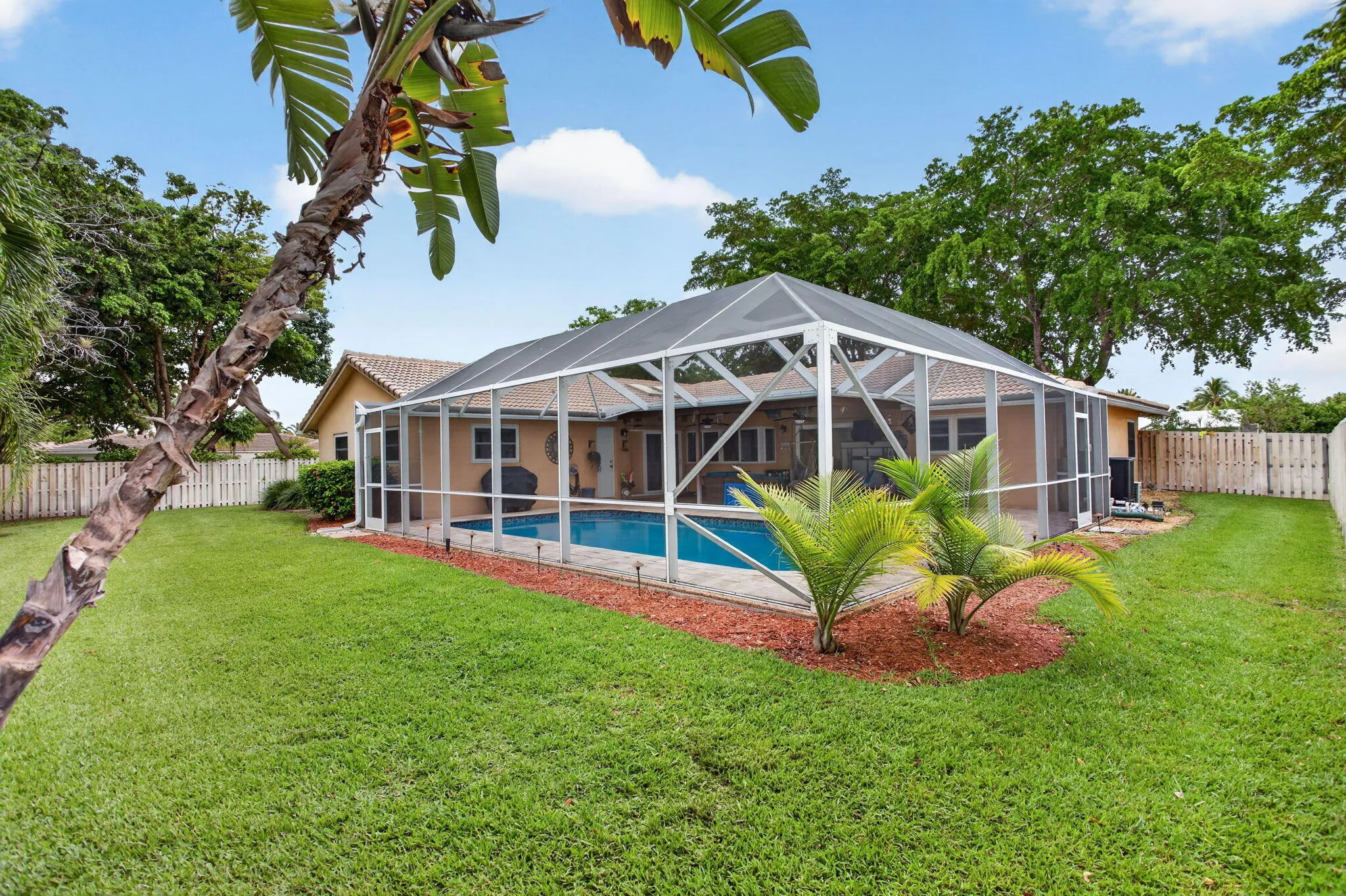Expansive backyard featuring a screened-in swimming pool, a privacy fence, and mature landscaping