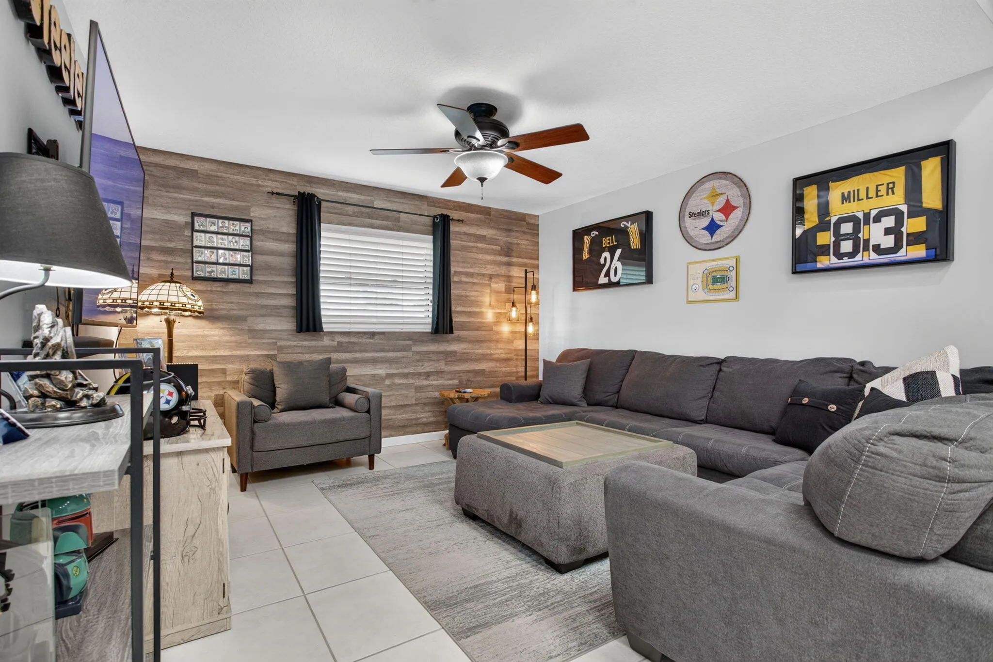 Wood-finish accent wall with two windows, ceiling fan with integrated lighting, and tile flooring
