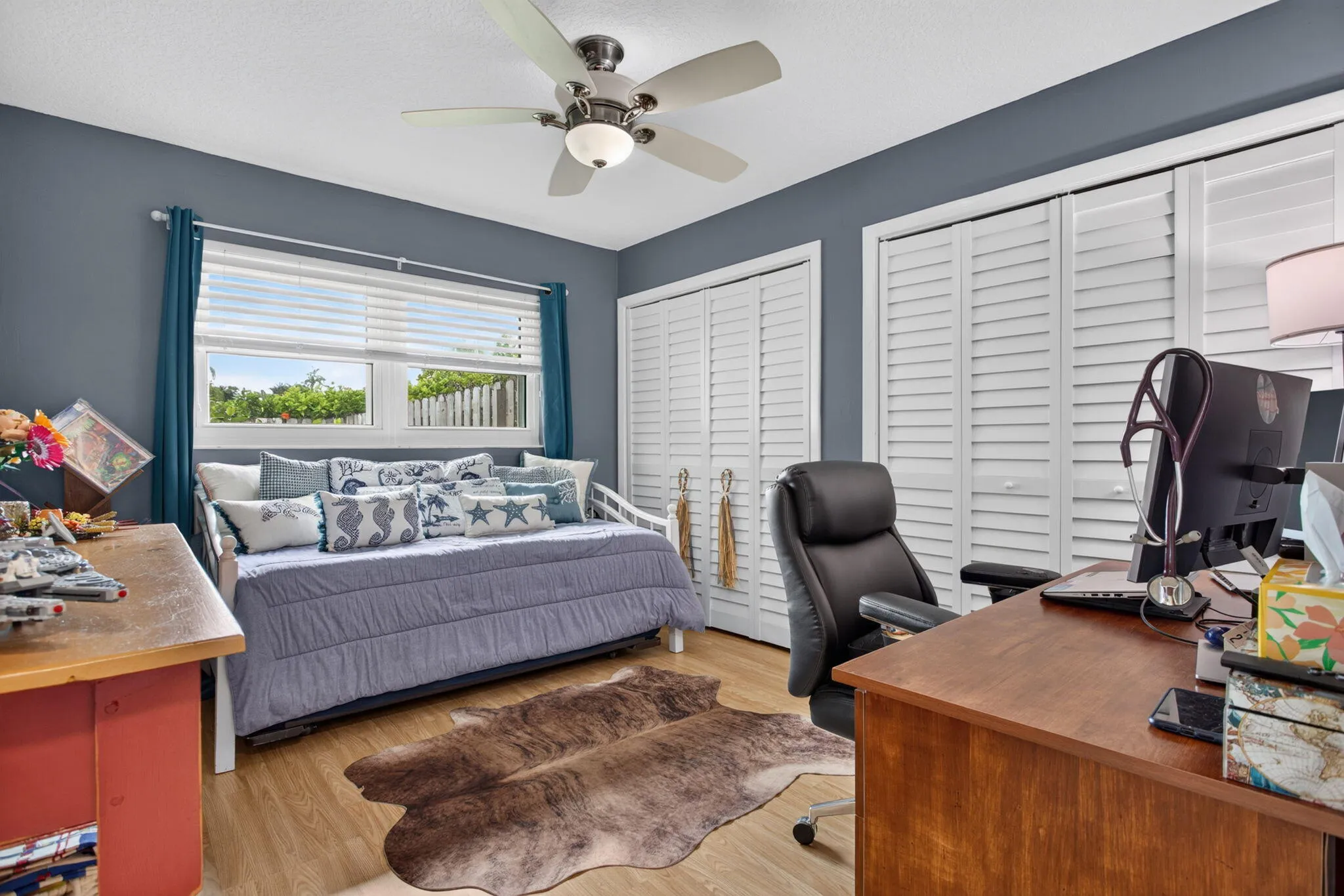 Room with wood-finish flooring, a ceiling fan with integrated lighting, and two sets of louvered bi-fold doors
