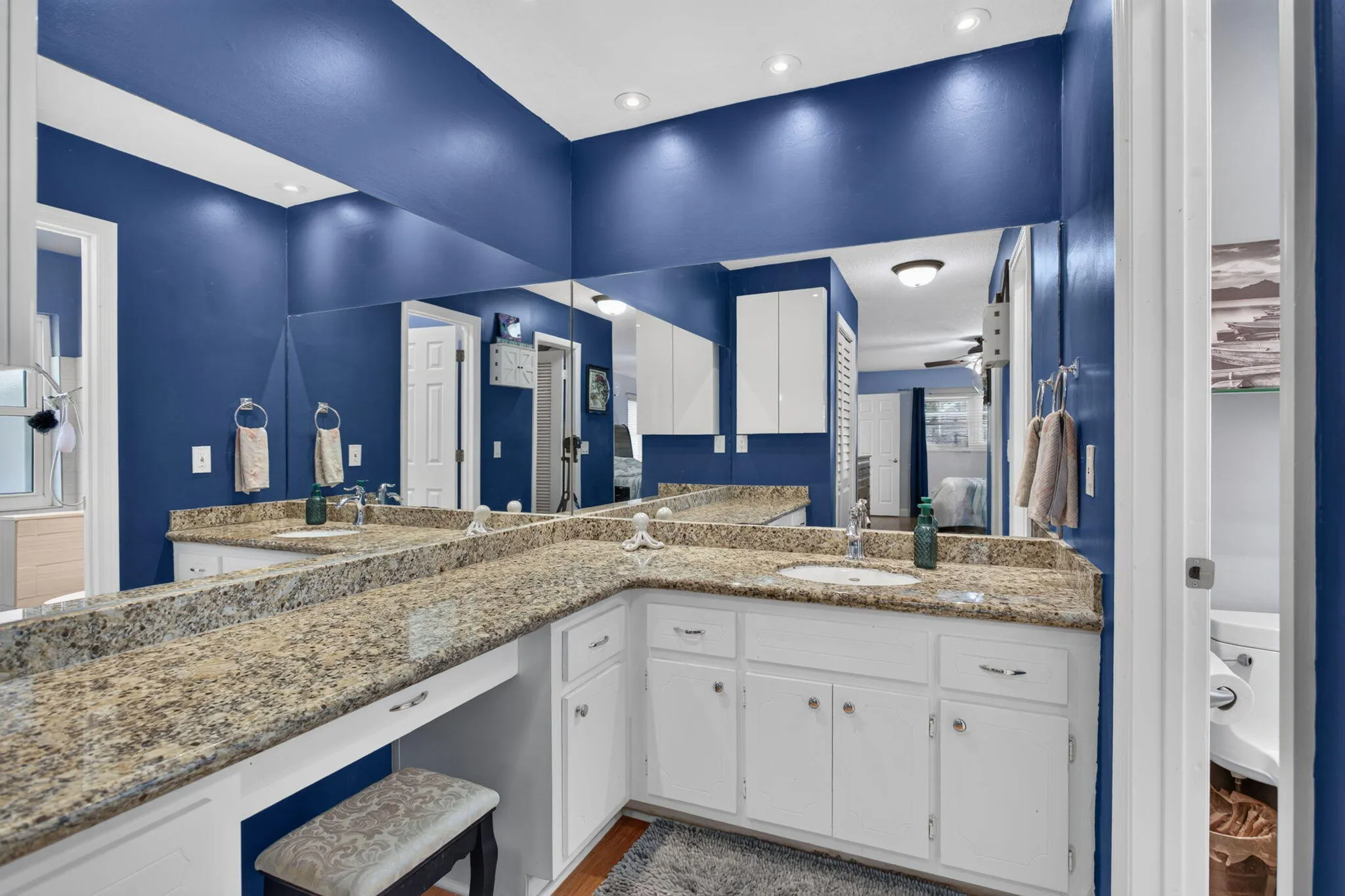 Granite-finish countertops, dual integrated sinks, white cabinetry, integrated vanity area, and wall-mounted mirrors