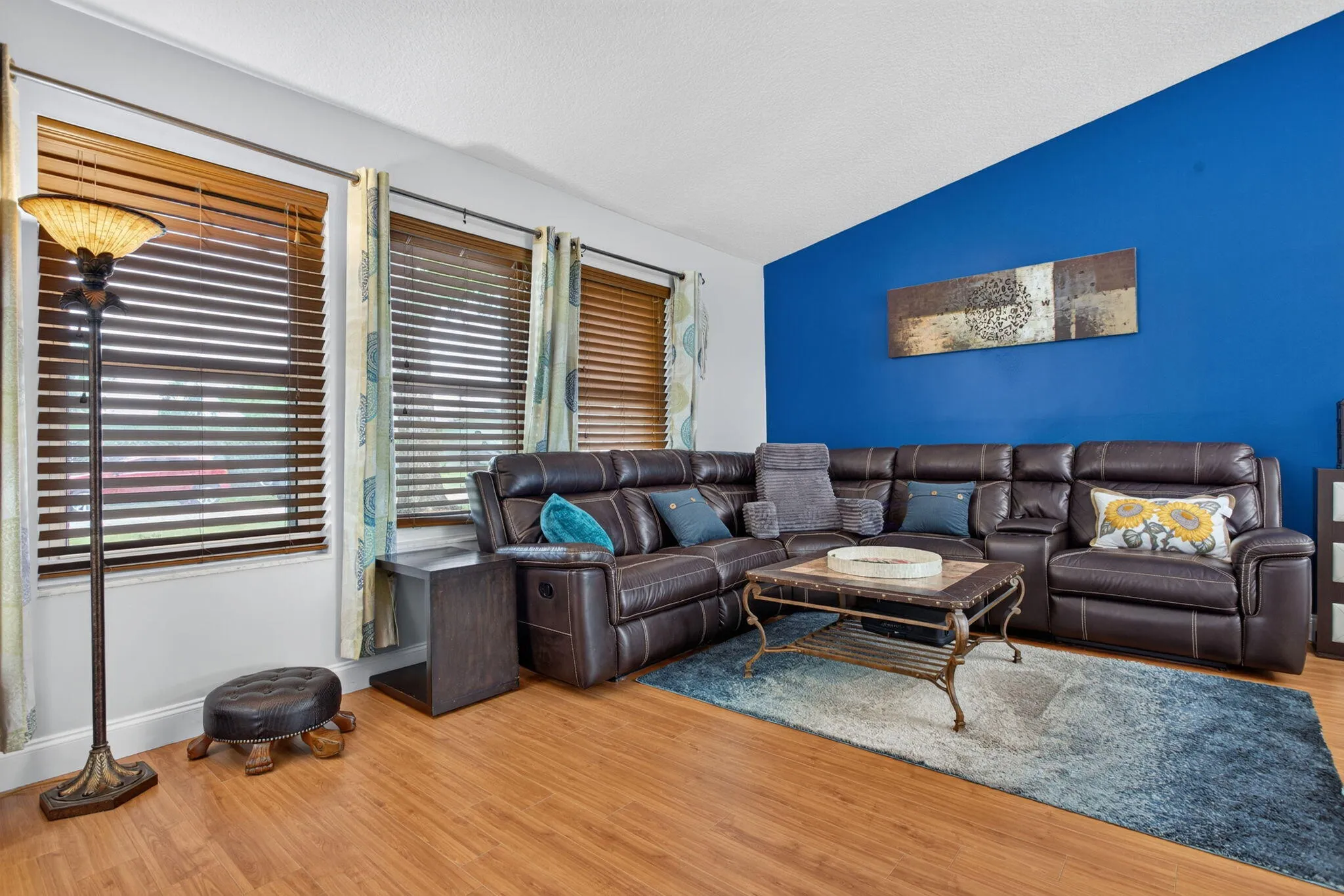 Wood-finish flooring throughout, complemented by multiple windows with wood blinds, and a distinctive accent wall