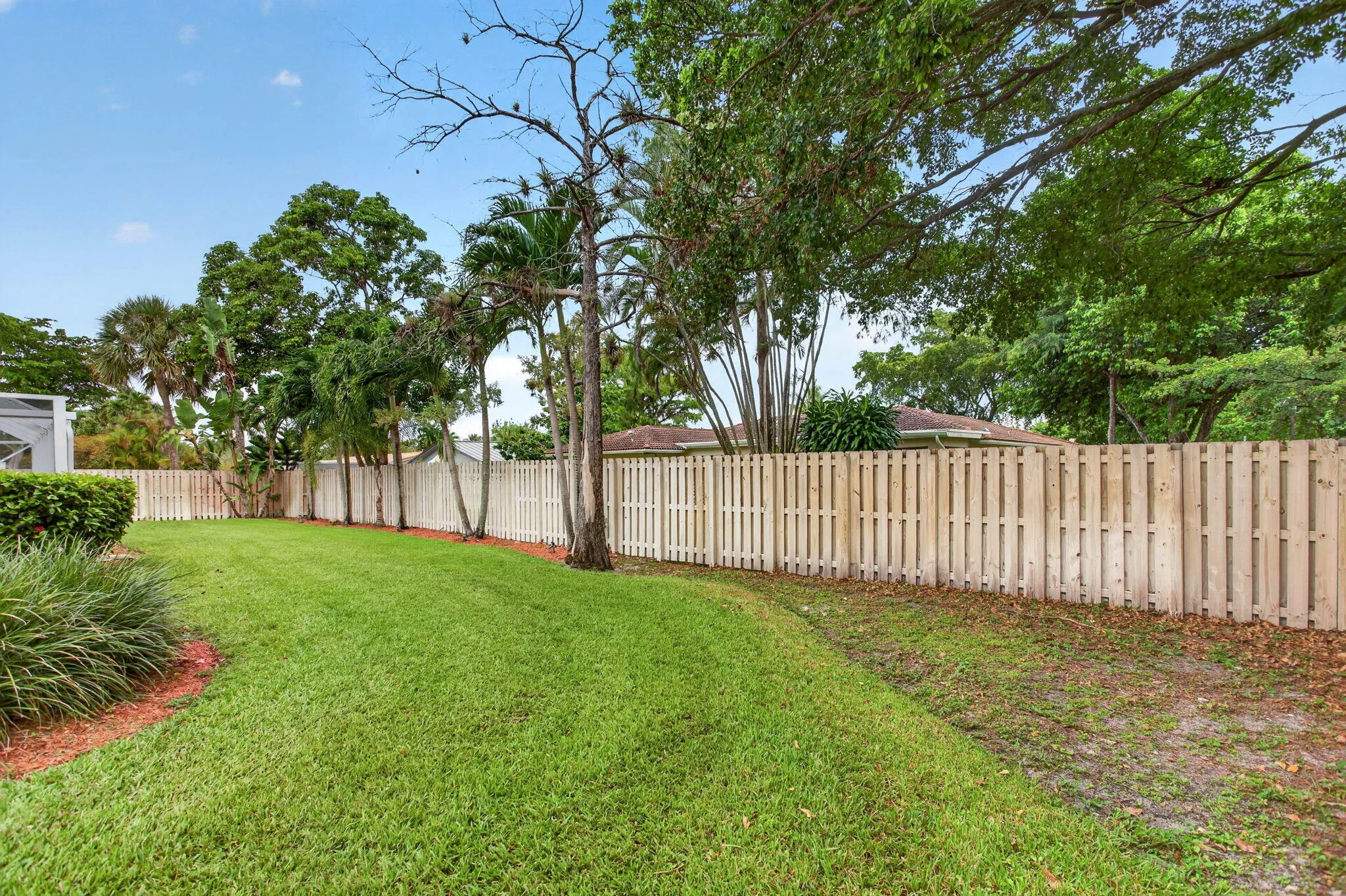 Expansive backyard featuring a privacy fence, mature trees, and natural landscaping
