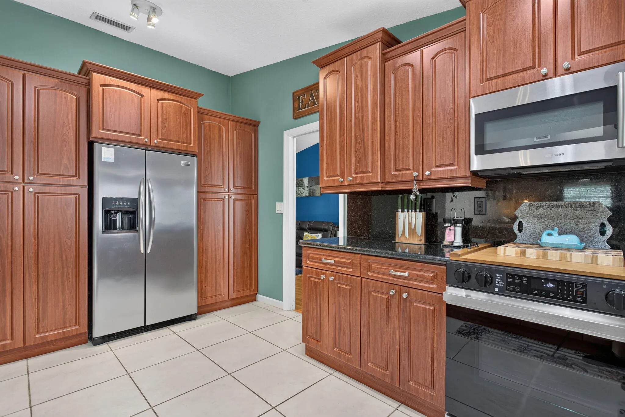 Expansive kitchen featuring abundant wood-finish cabinetry, stainless steel refrigerator, built-in microwave, and black granite countertops