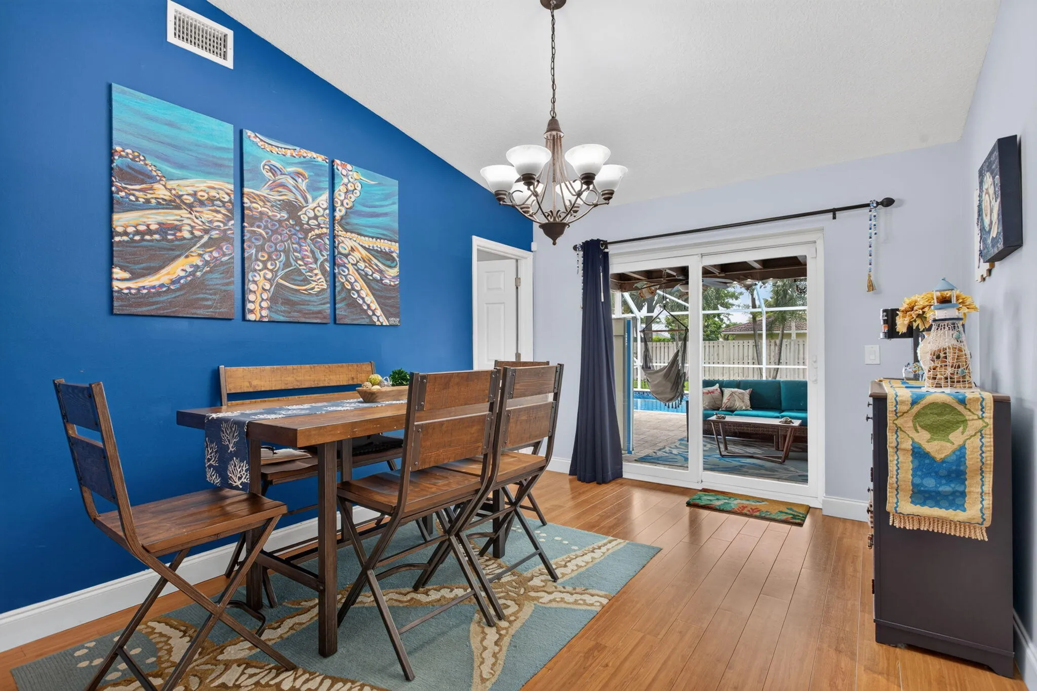 Wood-finish flooring with a multi-light chandelier, featuring a sliding glass door and transom window leading to an outdoor pool area
