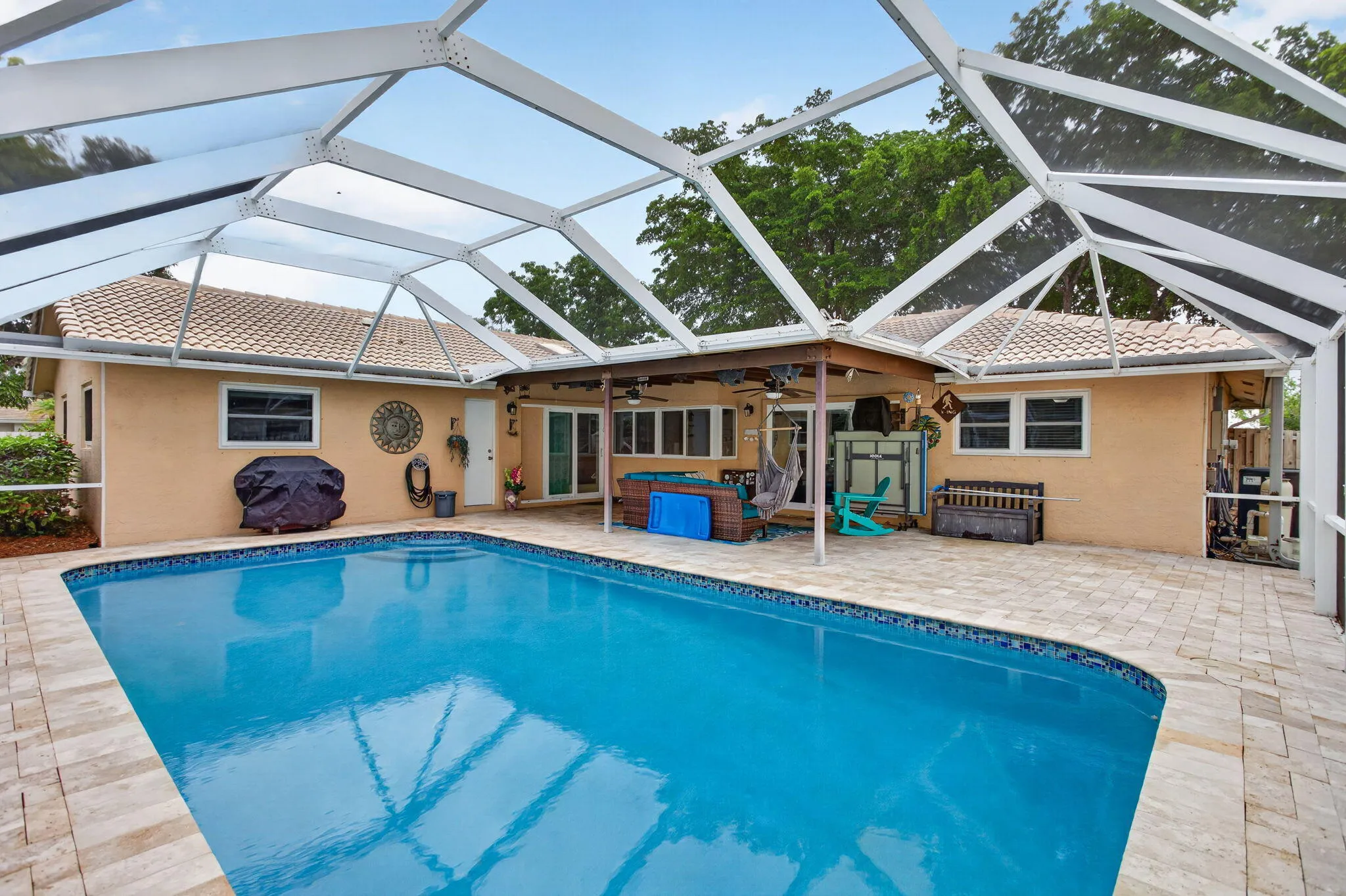 Screened-in pool enclosure featuring a rectangular pool with light blue water, surrounded by light-colored pavers