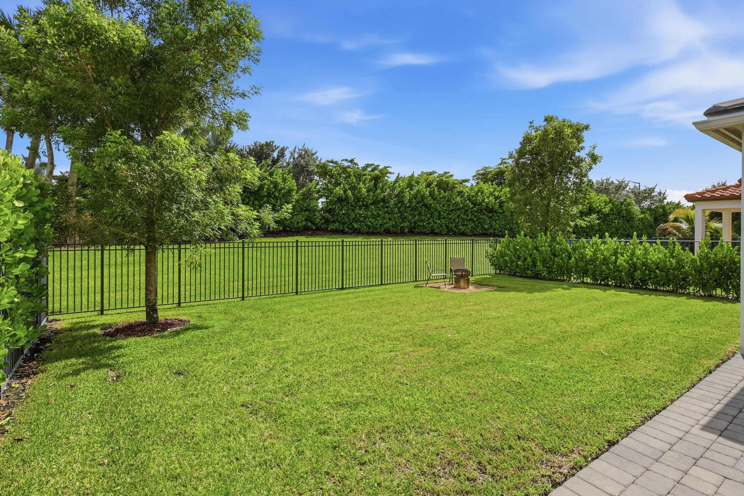 Expansive lawn bordered by a black metal fence and mature landscaping