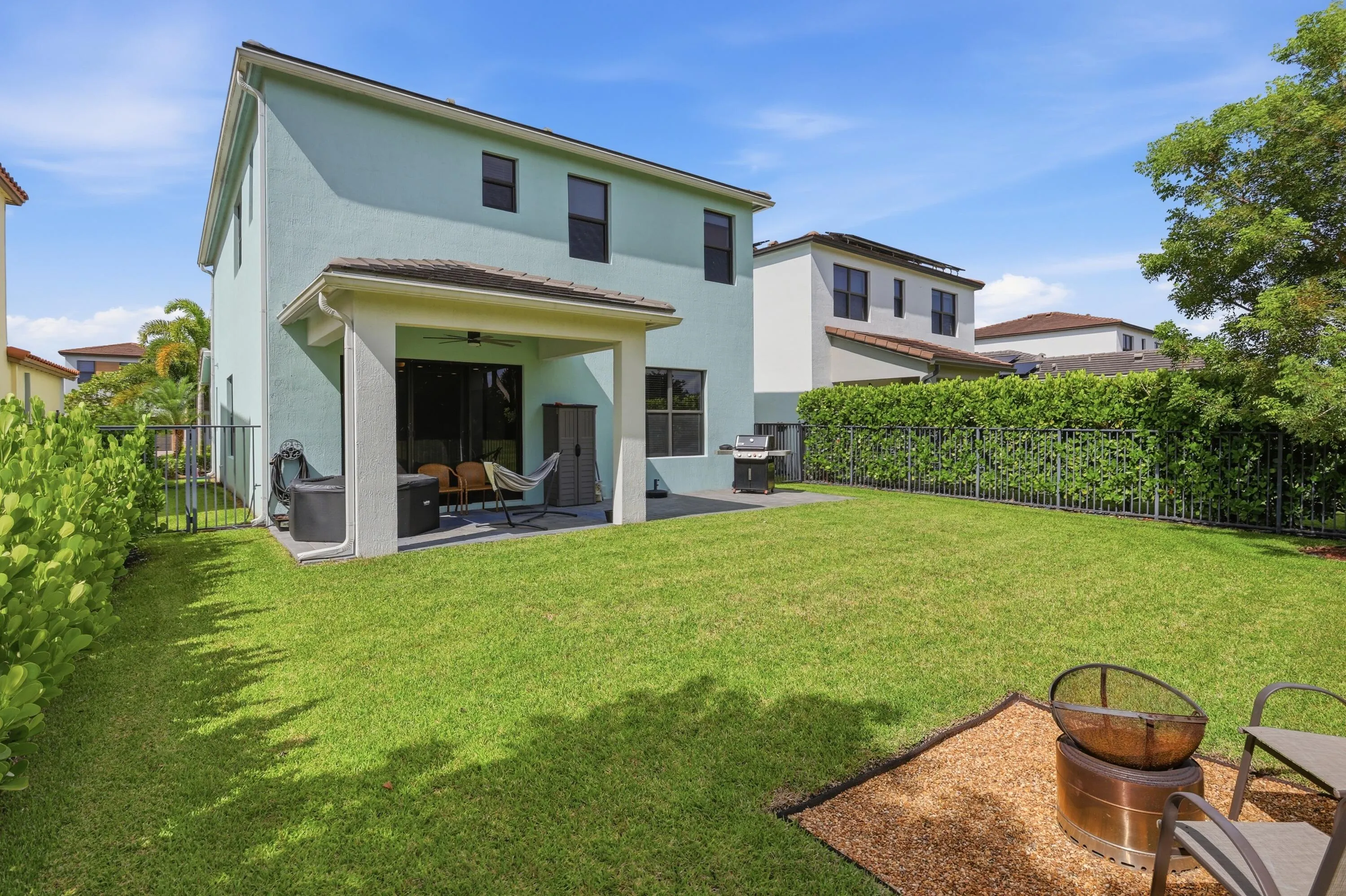 Expansive backyard with a covered patio, established lawn, and privacy hedging along the perimeter