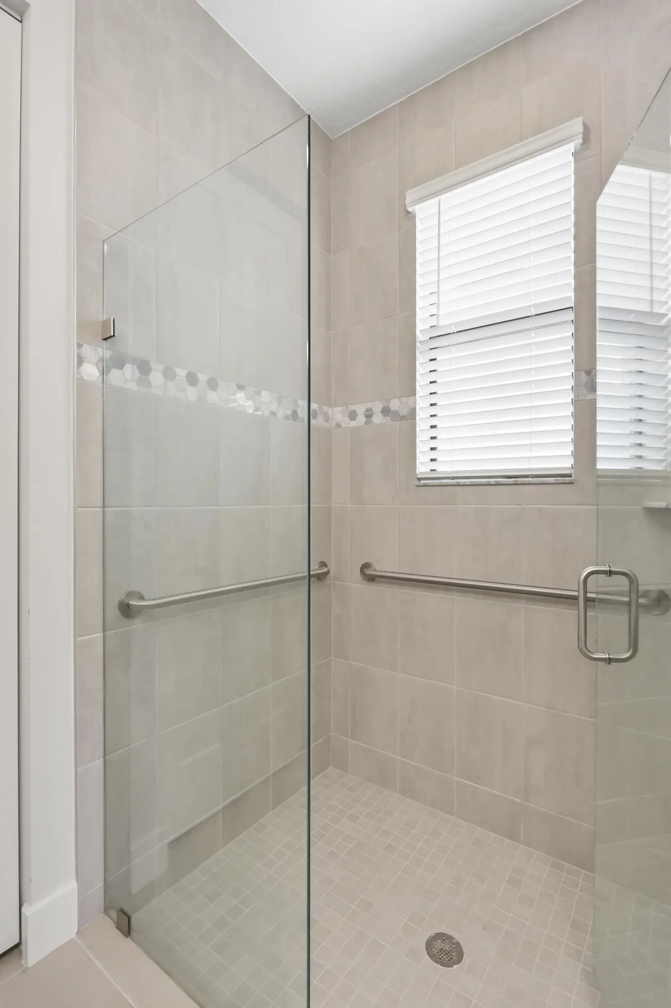 Glass-enclosed shower featuring large format wall tiles, mosaic accent tiling, and a tiled shower floor