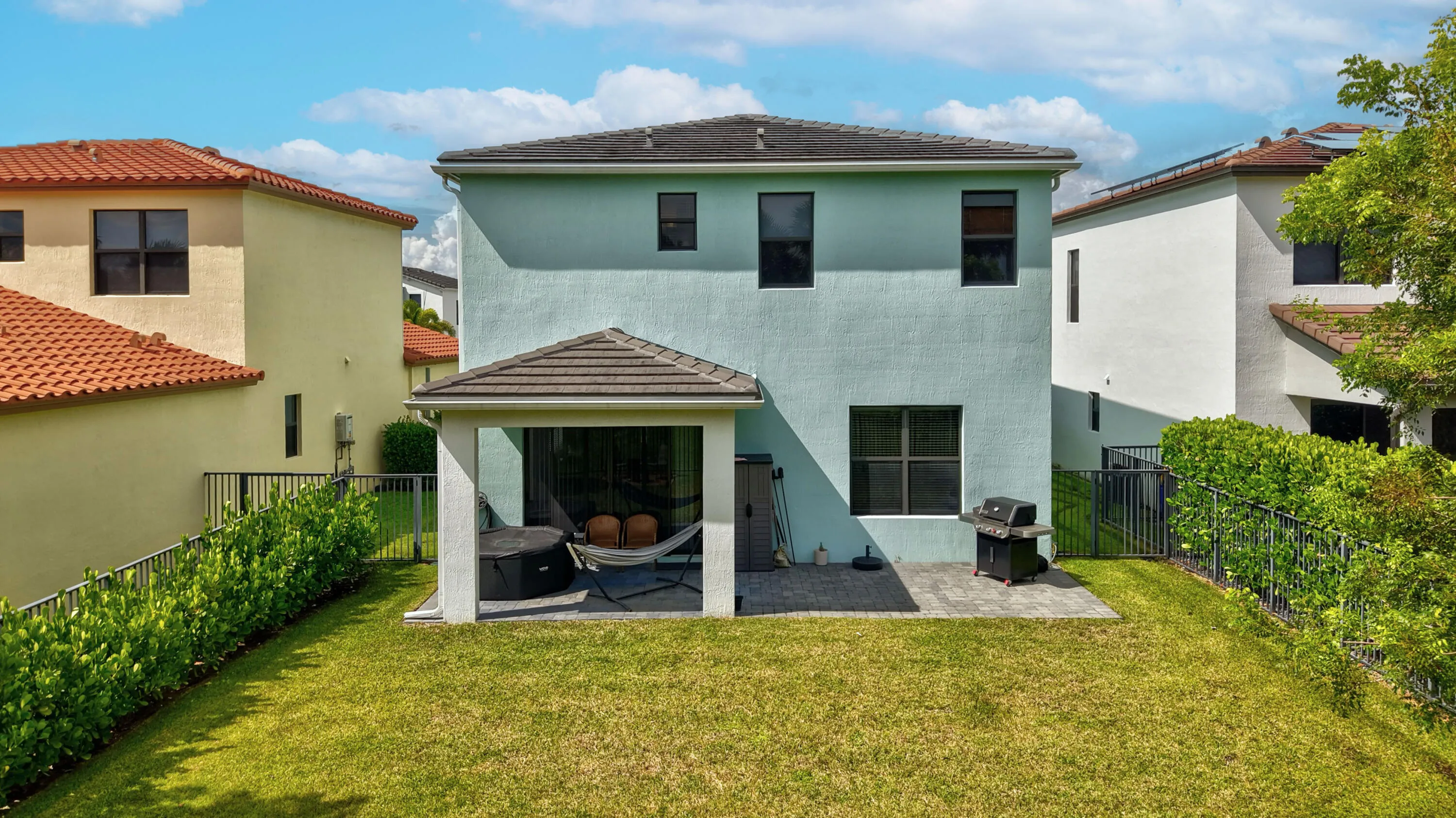 Expansive green lawn with a covered patio, paved outdoor area, and established perimeter hedging