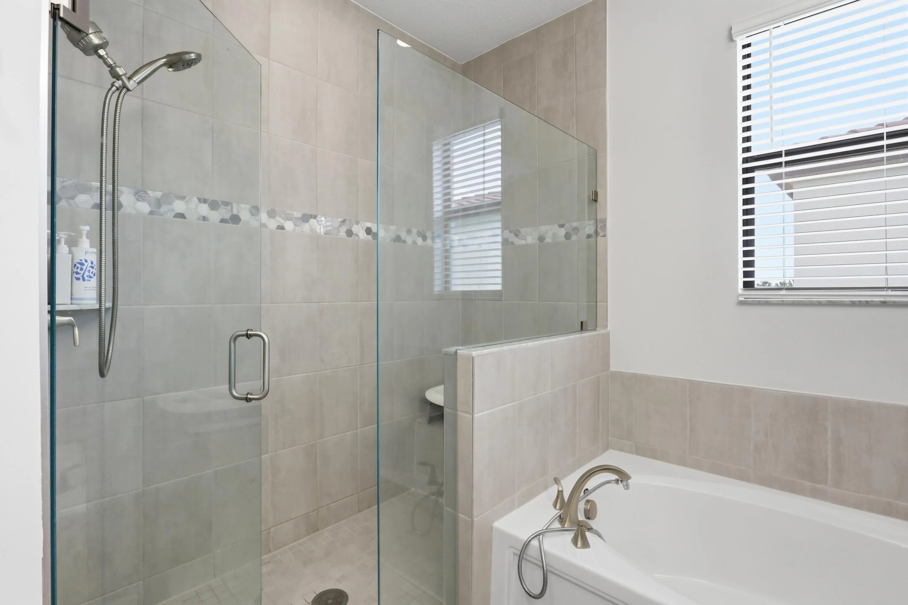 Glass-enclosed shower with a mosaic tile accent band, integrated shower niche, and brushed nickel fixtures