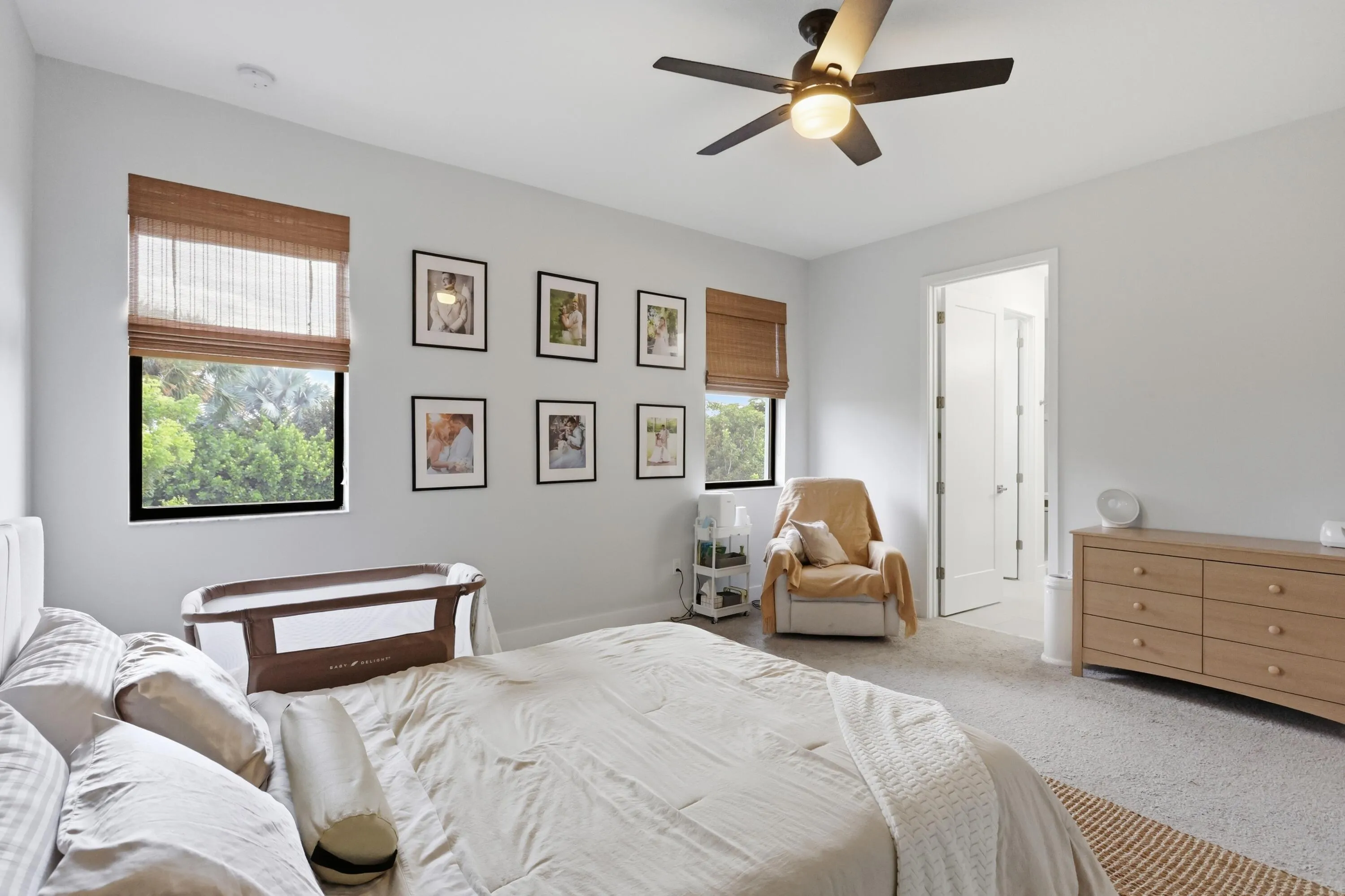 Recessed lighting, ceiling fan with integrated light, two windows with woven shades, and light-toned carpeting