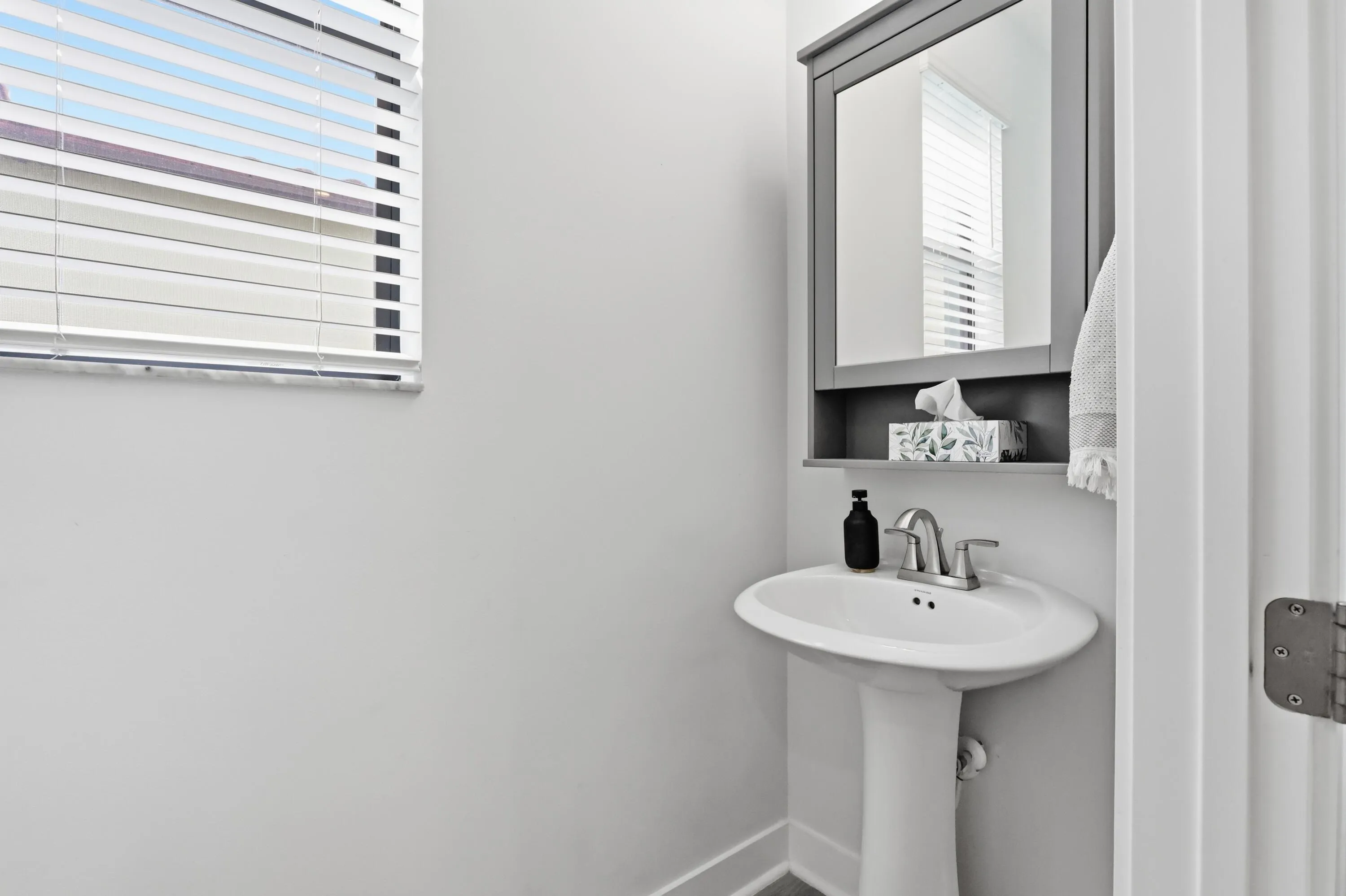 Pedestal sink with a two-handle faucet, mirrored medicine cabinet, and a window with blinds