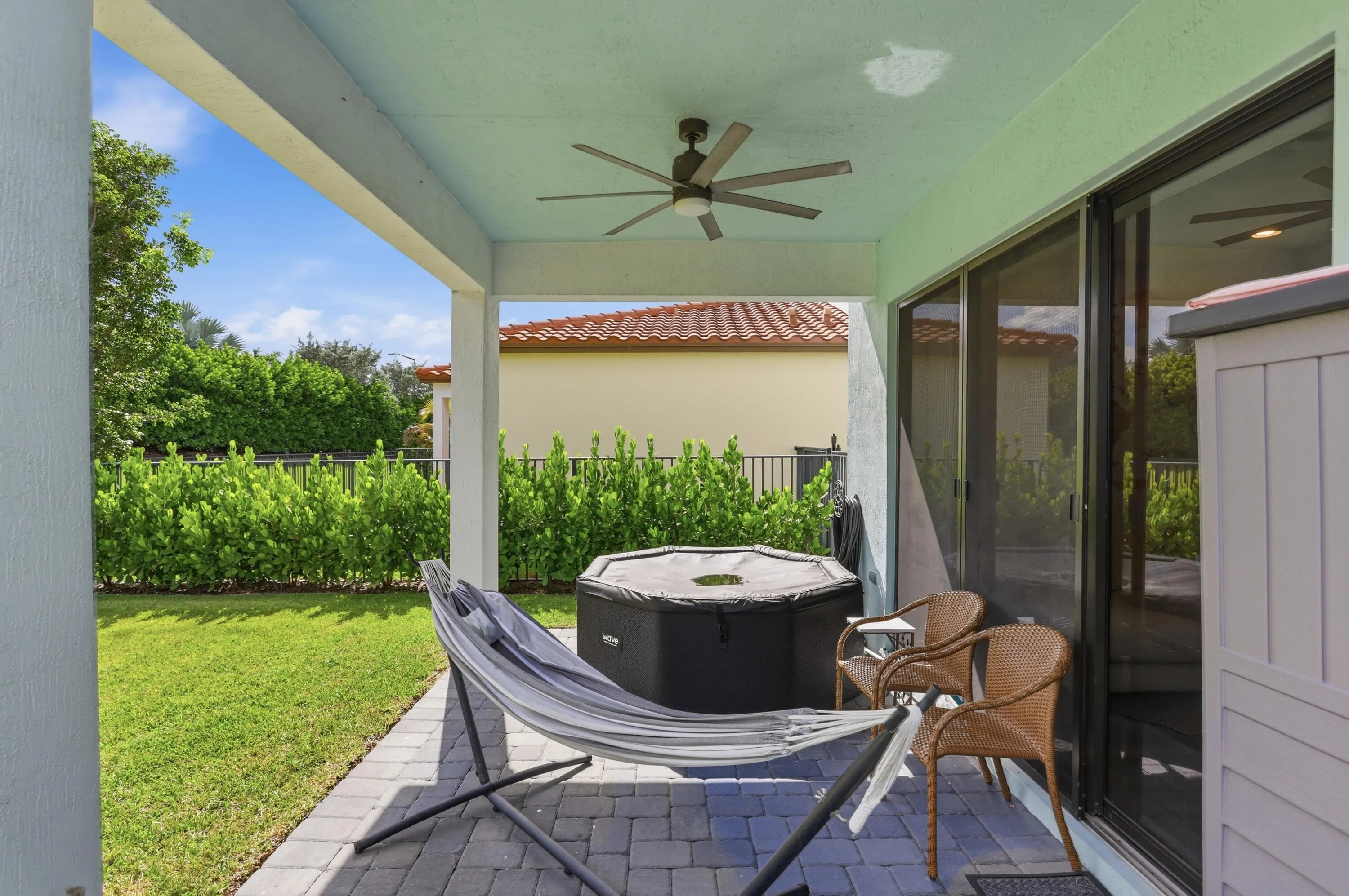 Covered patio with a ceiling fan, paved flooring, and sliding glass doors