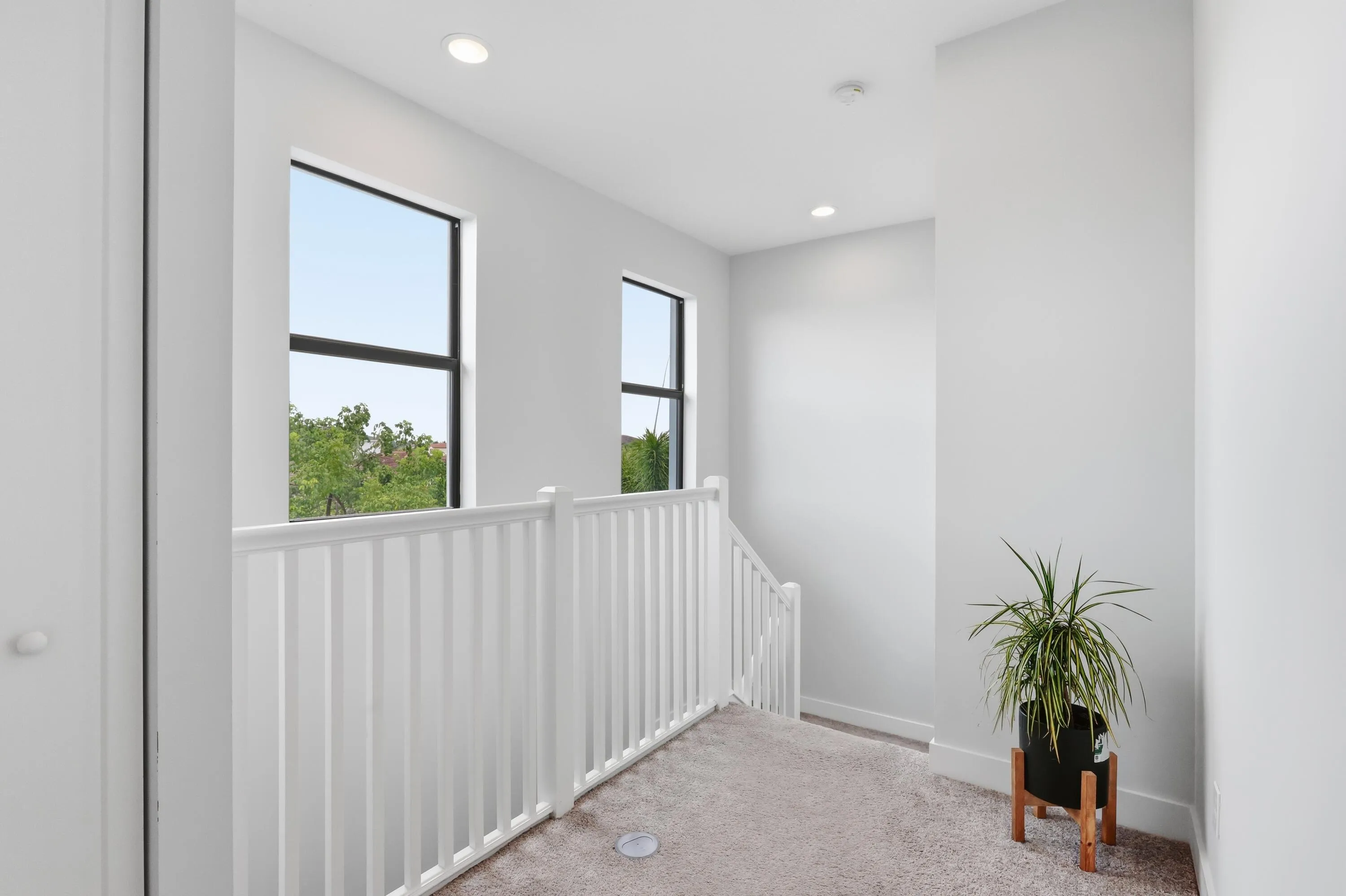 Carpeted hallway with white railing, recessed lighting, and dual windows