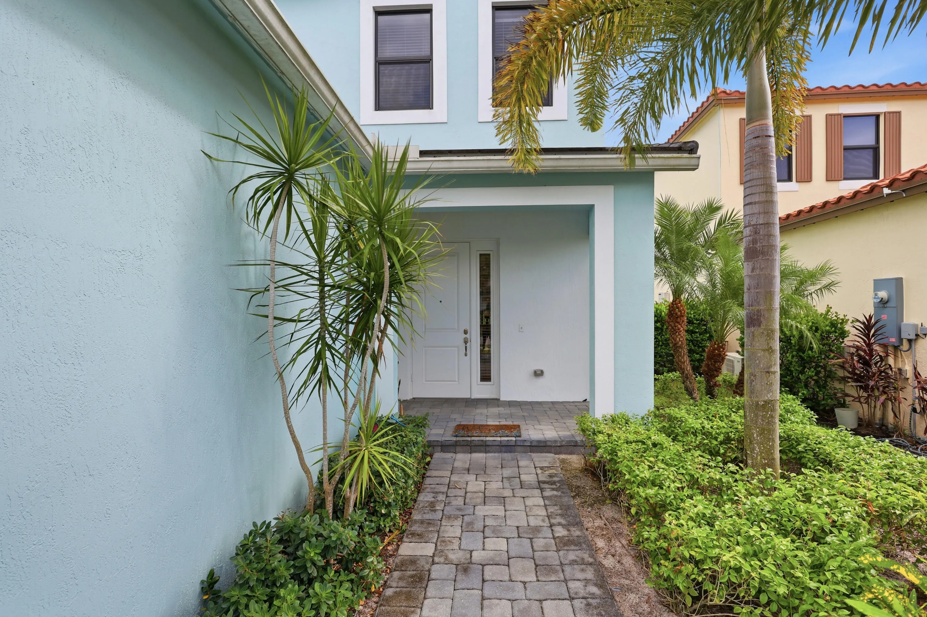 Entryway with a paved walkway, covered porch, and lush landscaping