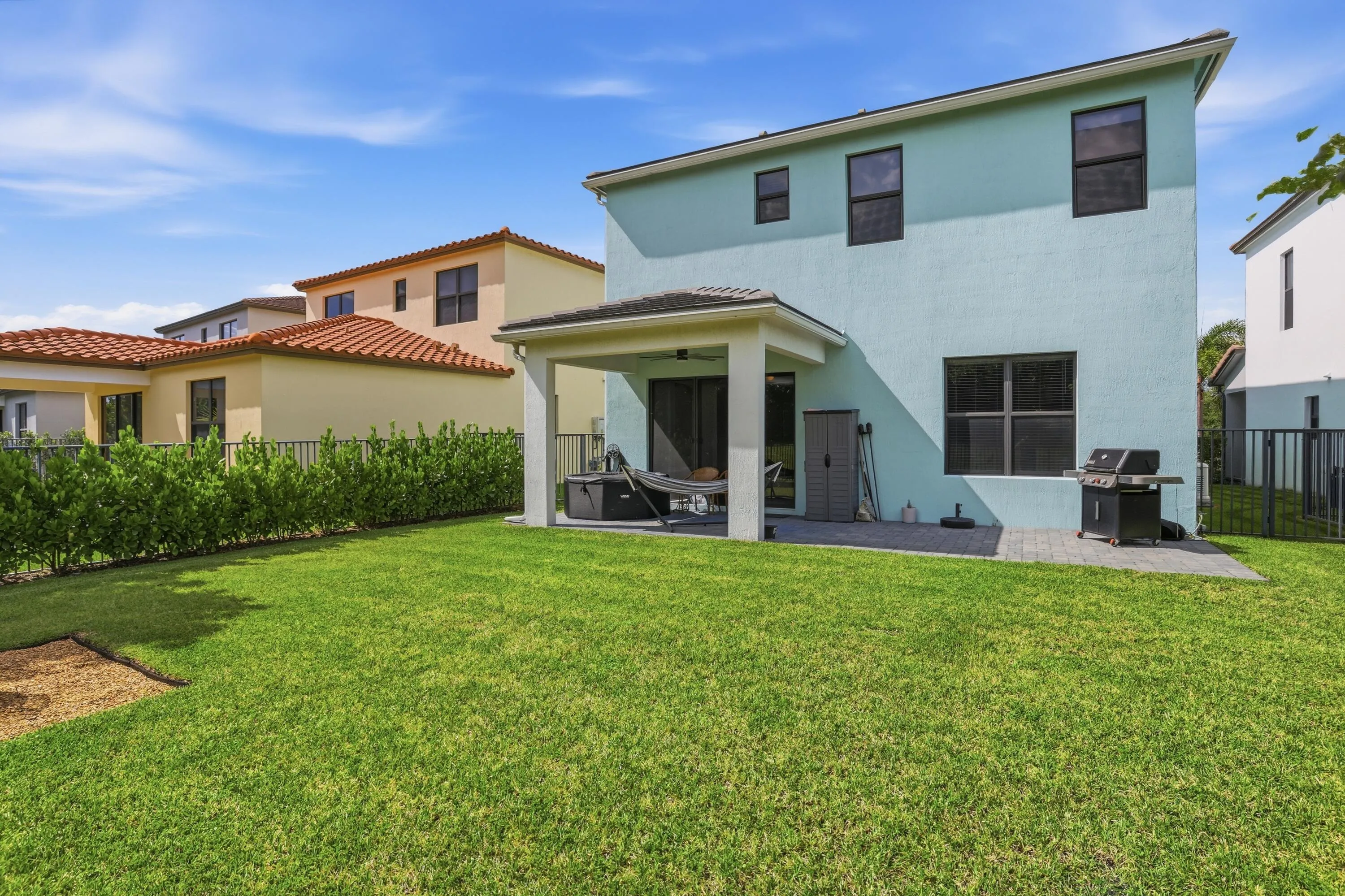 Expansive backyard featuring a manicured lawn, covered patio, and privacy hedging