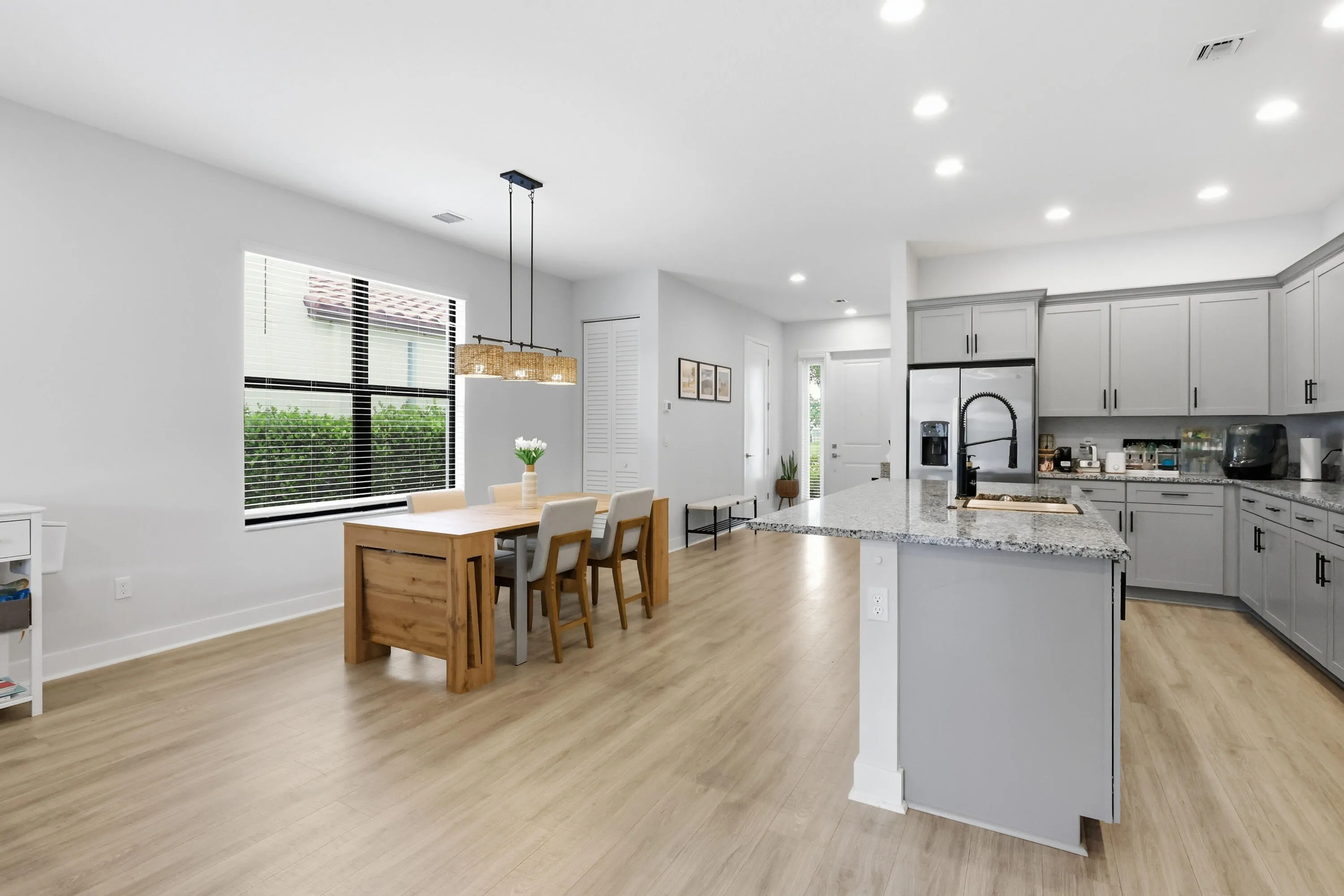 Open-concept living area with wood-finish flooring, a contemporary kitchen featuring light grey cabinetry, stainless steel appliances, and a central island with a stone countertop