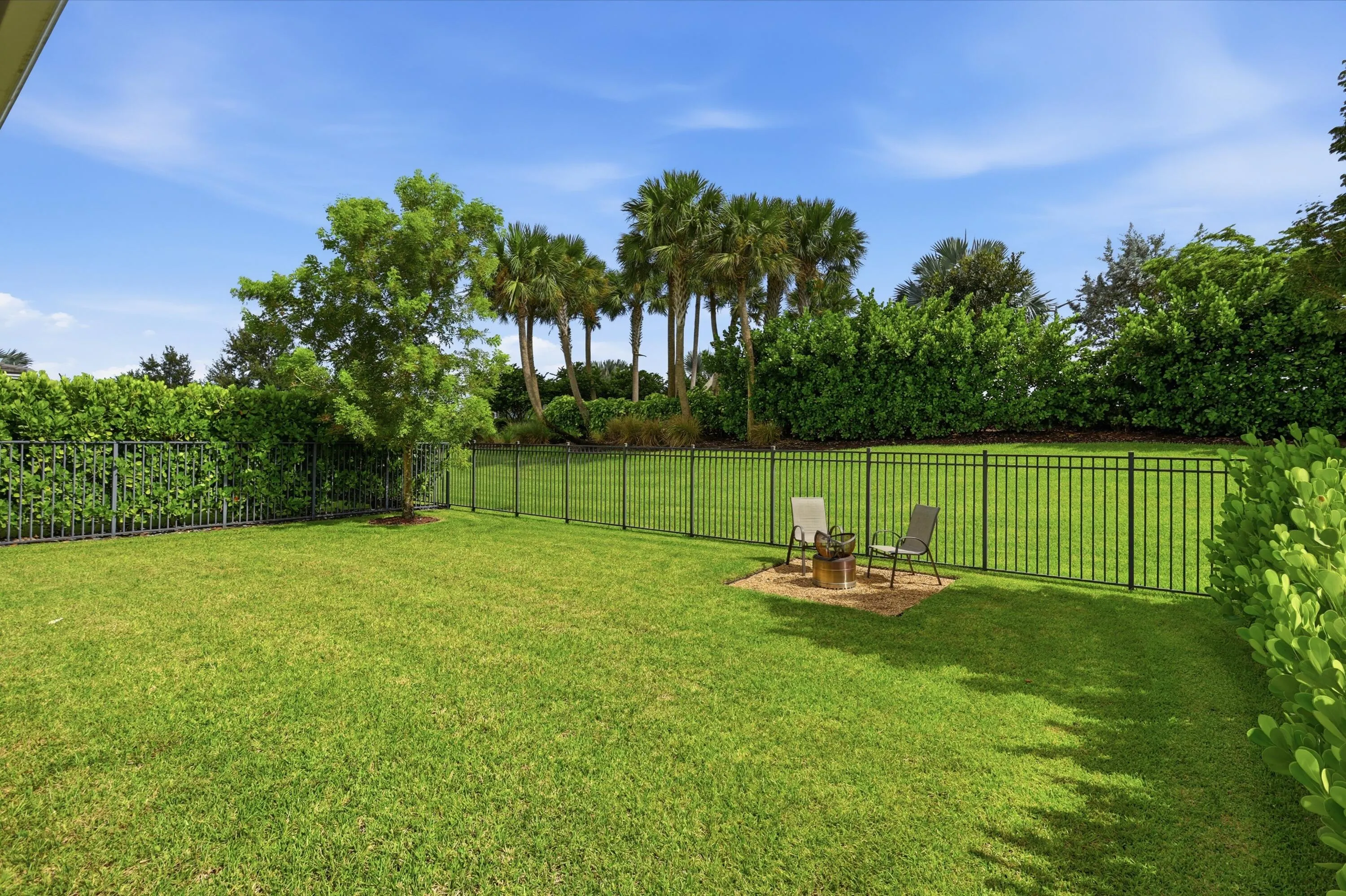 Expansive green lawn featuring a black metal perimeter fence and mature landscaping