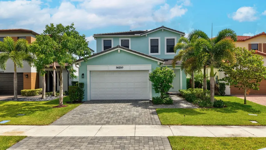 Two-story residence featuring a tile roof, a paver driveway, an integrated garage, and mature landscaping