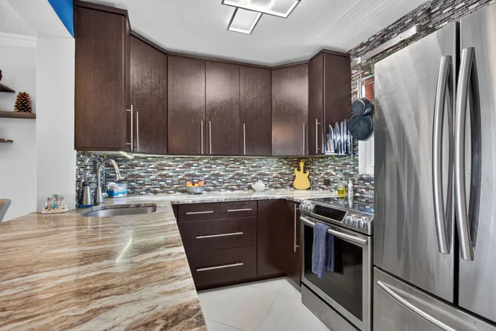 Rich wood-finish cabinetry, stainless steel appliances, mosaic tile backsplash, and a patterned countertop