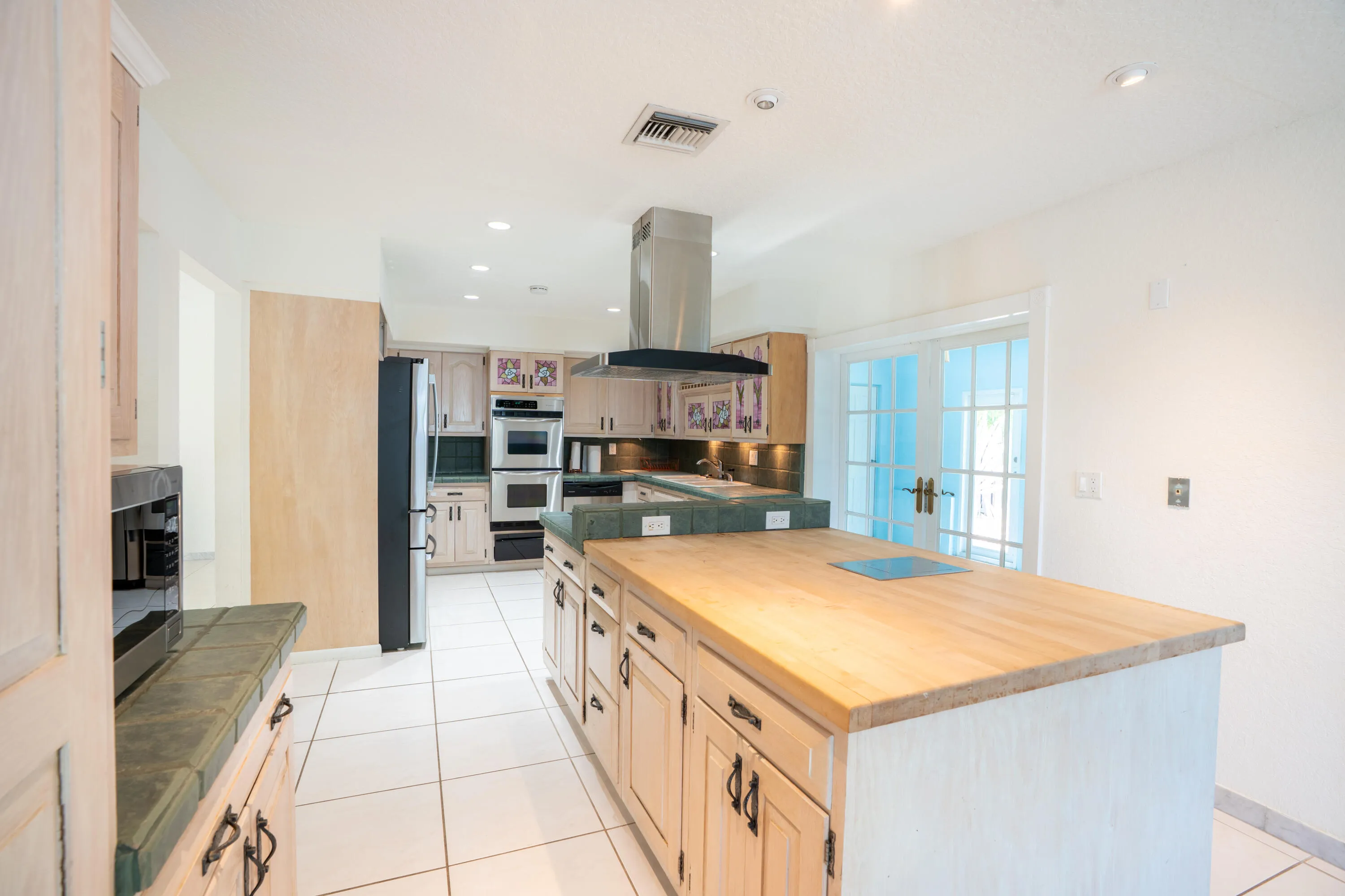 Expansive kitchen featuring a central island with a wood countertop, integrated cooktop, double wall ovens, and stainless steel range hood