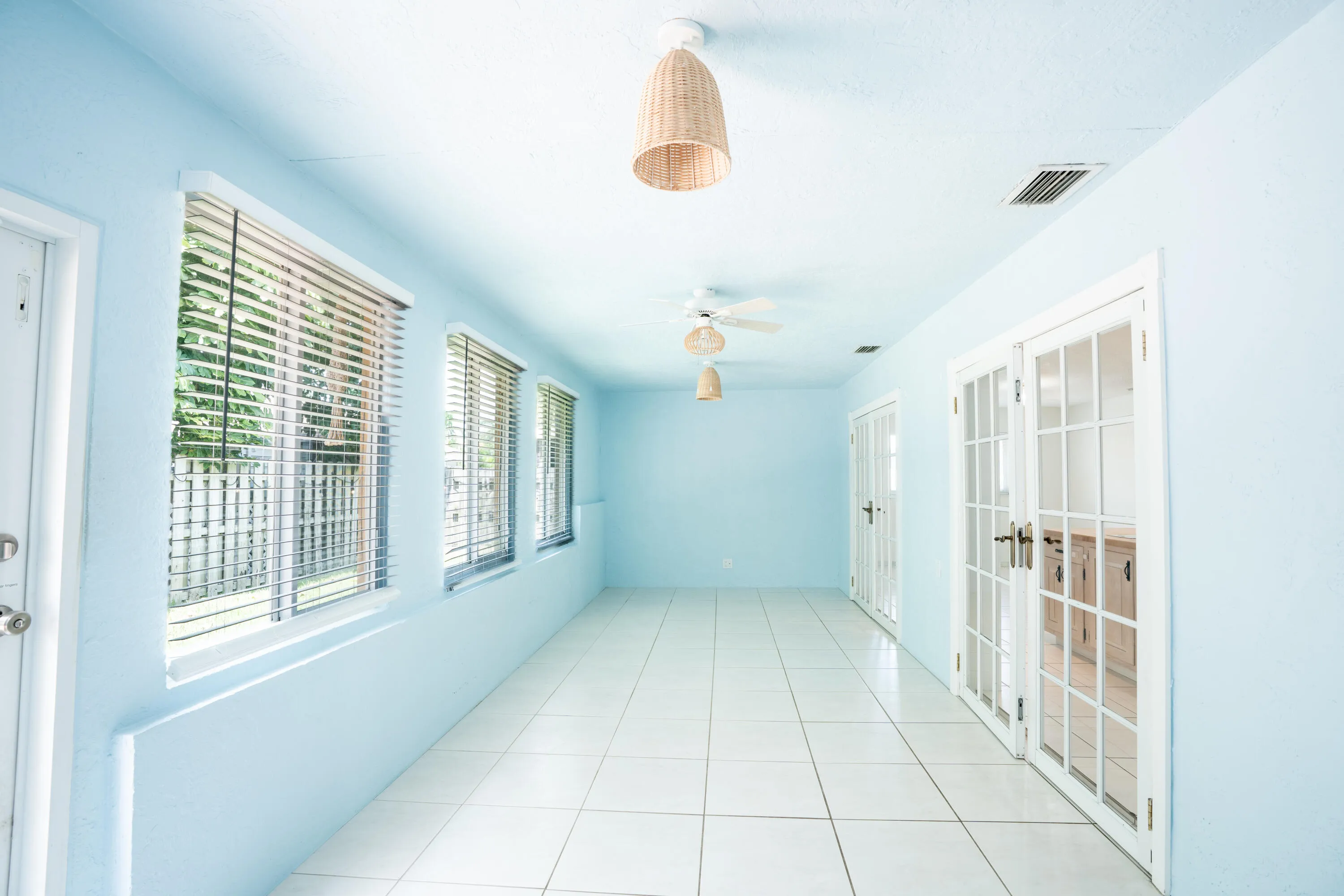 Long hallway with large windows, white tile flooring, and multiple sets of French doors