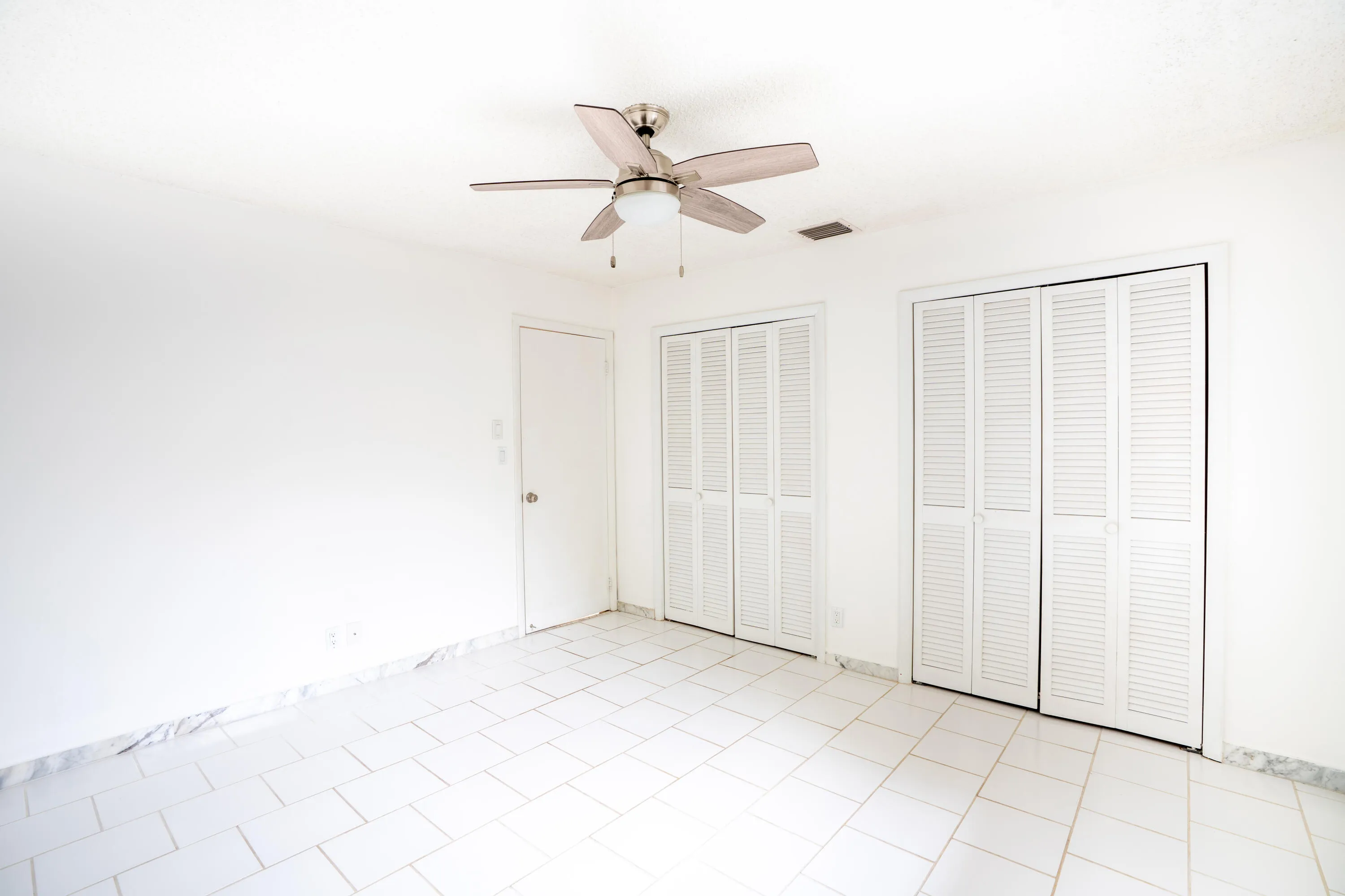 White tile flooring, clean white walls, two sets of louvered bifold closet doors, and a ceiling fan with integrated lighting