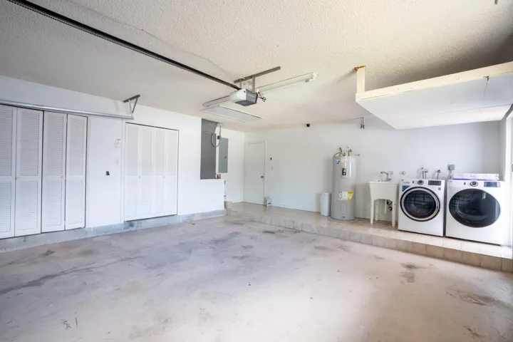 Spacious garage with polished concrete flooring, white overhead sectional door, ceiling fan, and dedicated laundry alcove featuring side-by-side washer and dryer units