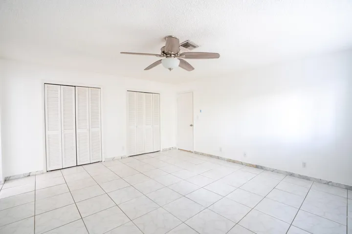 White tiled flooring, dual louvered bifold closet doors, and ceiling fan with integrated lighting