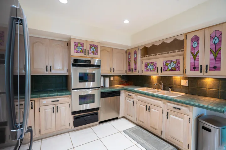 Stainless steel double oven, stainless steel refrigerator, stainless steel dishwasher, tile flooring, and custom cabinetry with stained glass inserts