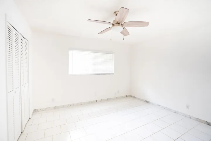 White tile flooring with a marble-finish border, white walls, and a window with horizontal blinds