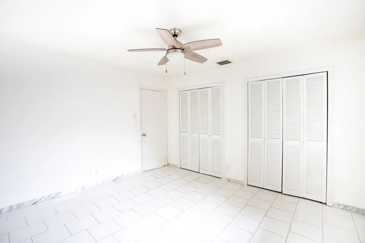 White tile flooring, clean white walls, two sets of louvered bifold closet doors, and a ceiling fan with integrated lighting