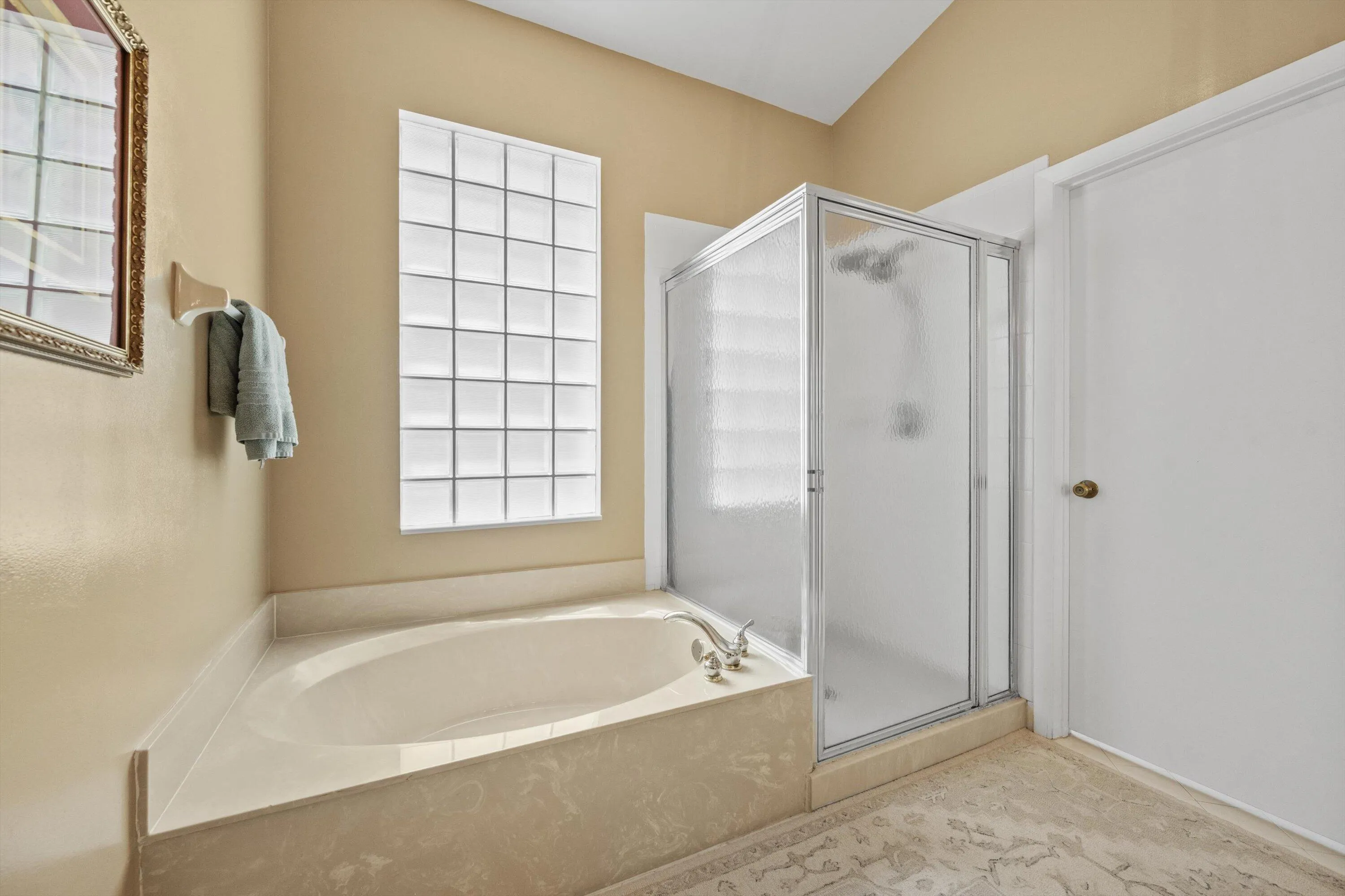 Built-in soaking tub, glass block window, enclosed shower, and beige wall paint