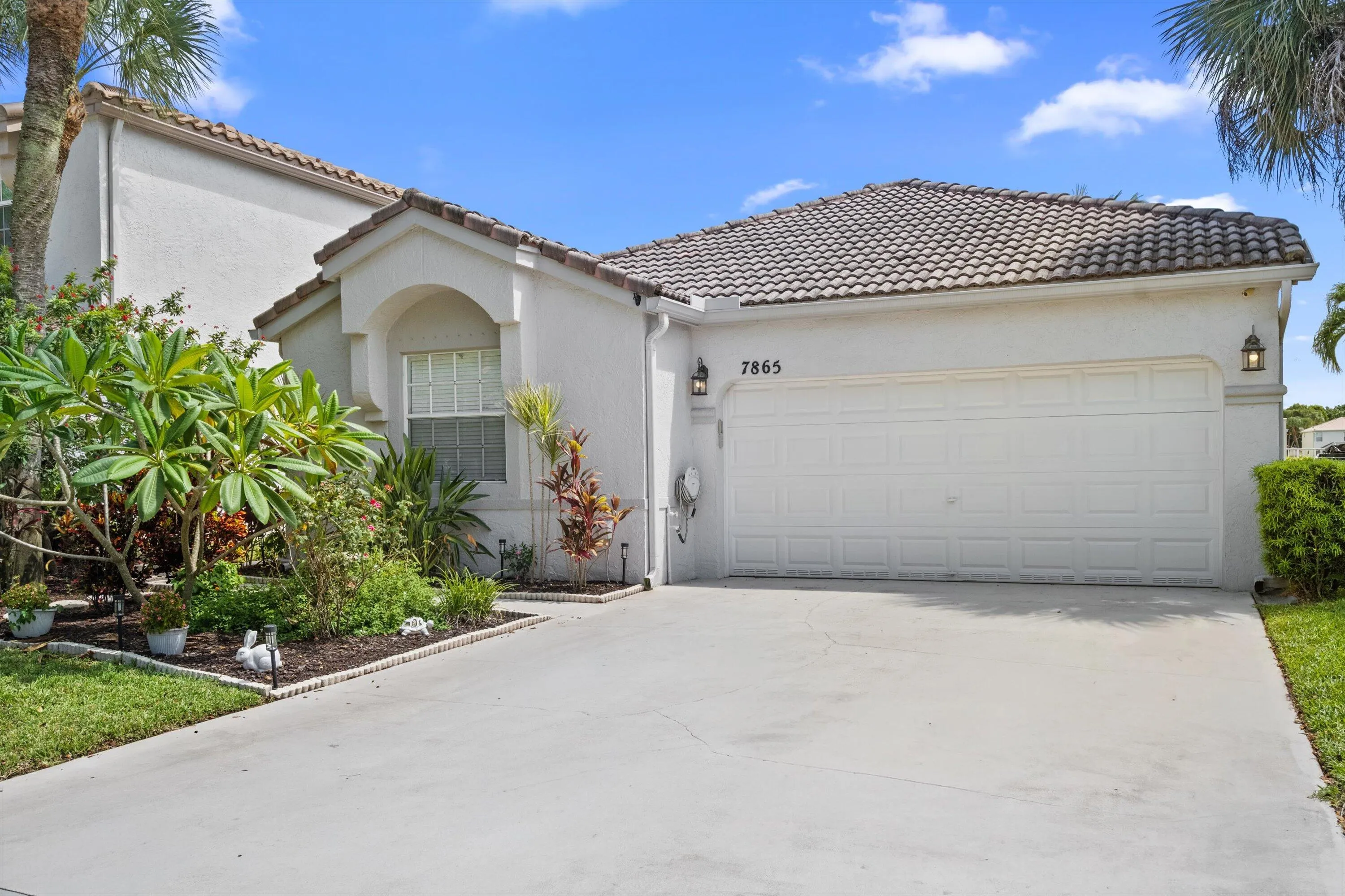 Stucco exterior with a tile roof, an integrated garage, a concrete driveway, and established landscaping