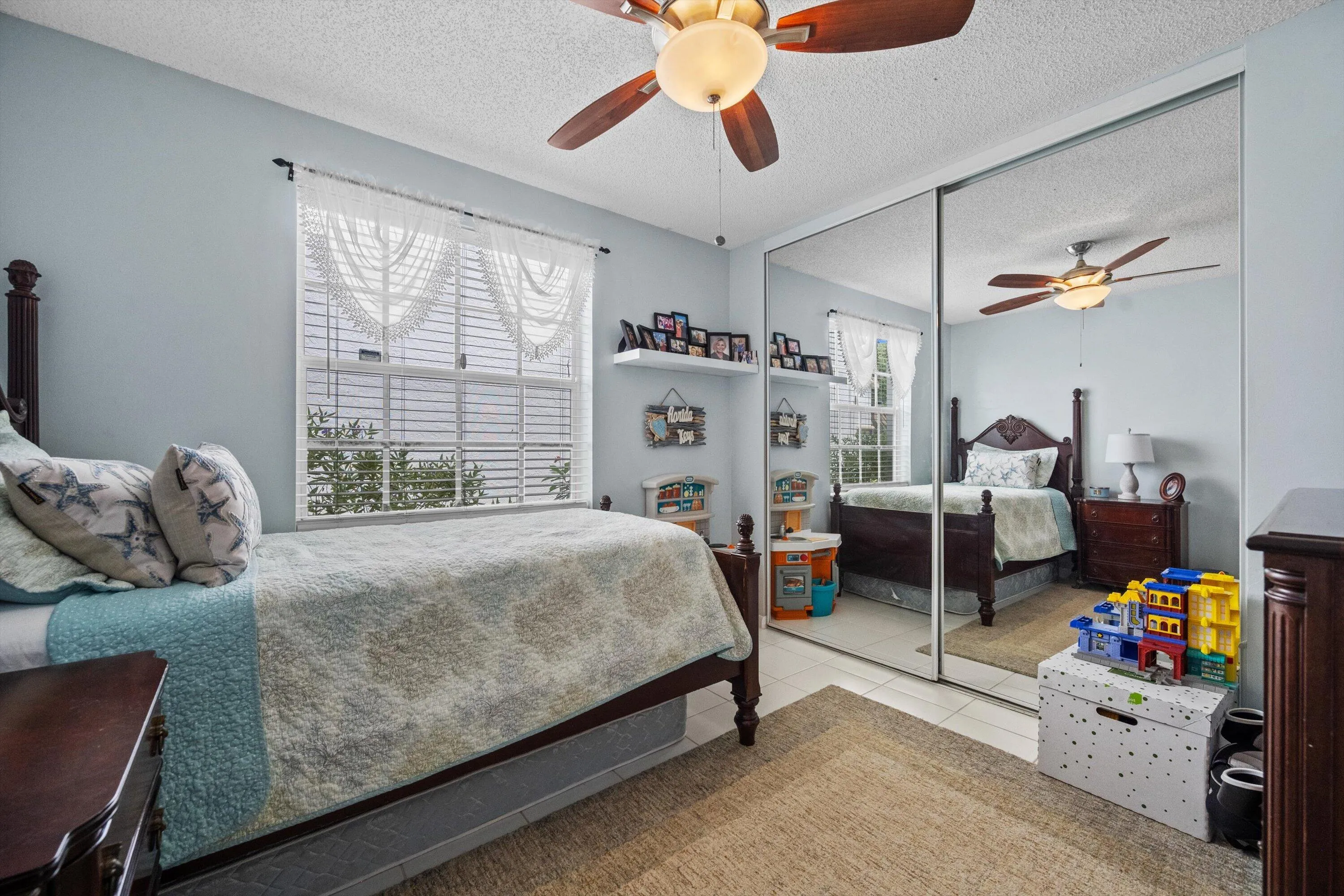 White tile flooring with a neutral area rug, a ceiling fan with integrated lighting, and mirrored closet doors