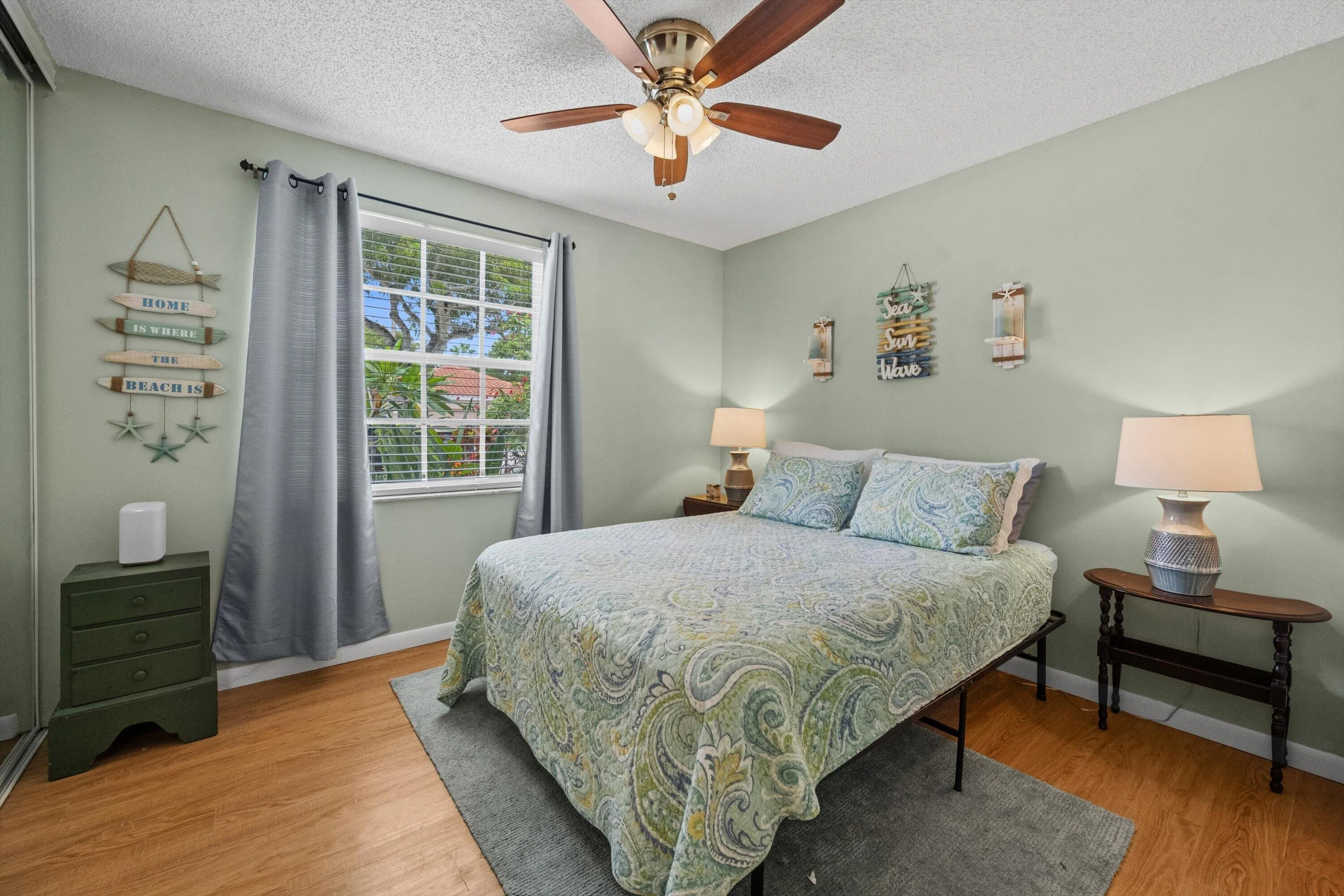 Window with horizontal blinds, wood-finish flooring, ceiling fan with integrated lighting, wall-mounted light fixtures, and a built-in closet with mirrored sliding doors