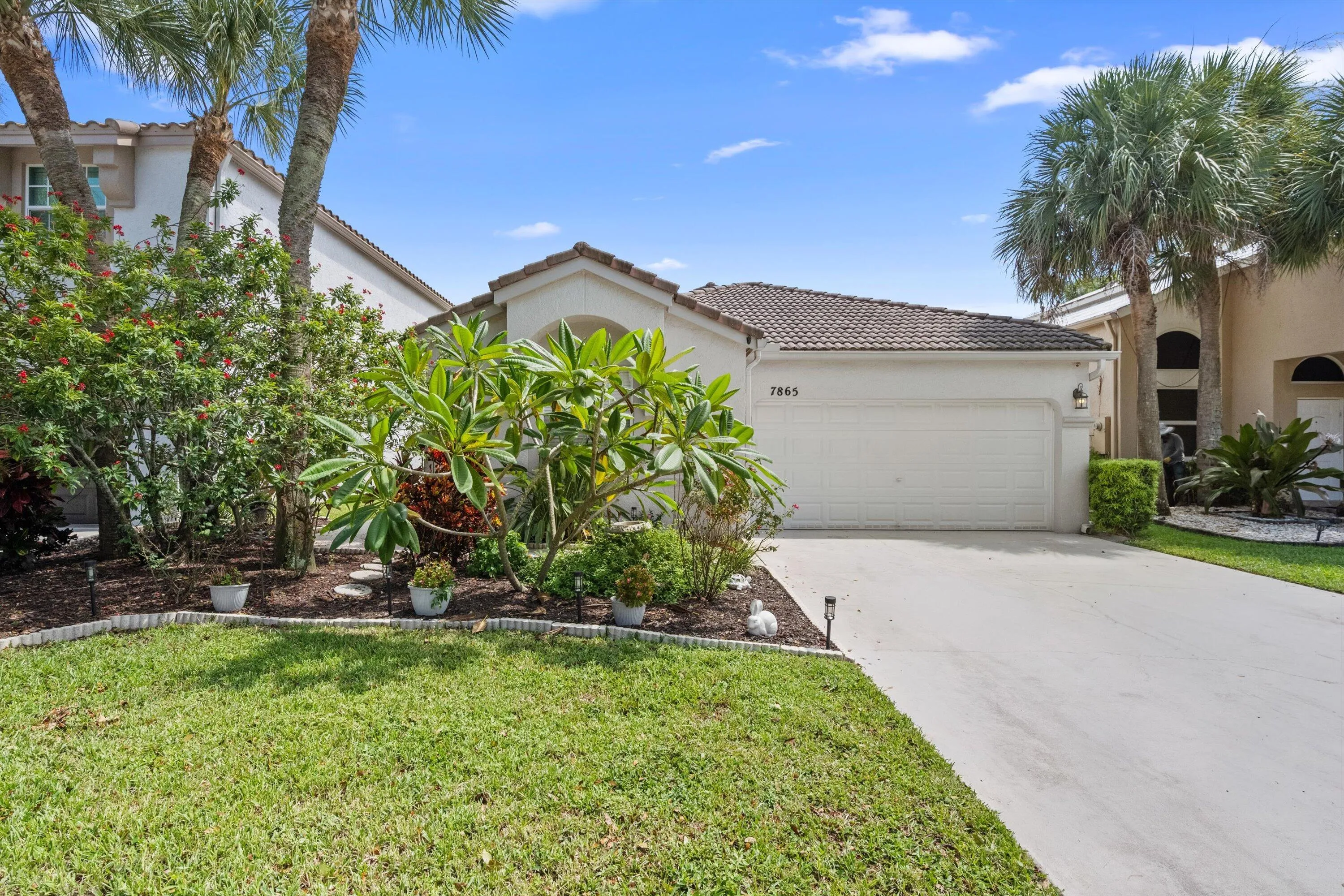 Stucco exterior featuring a tiled roof, attached garage, concrete driveway, and landscaped front yard with mature trees